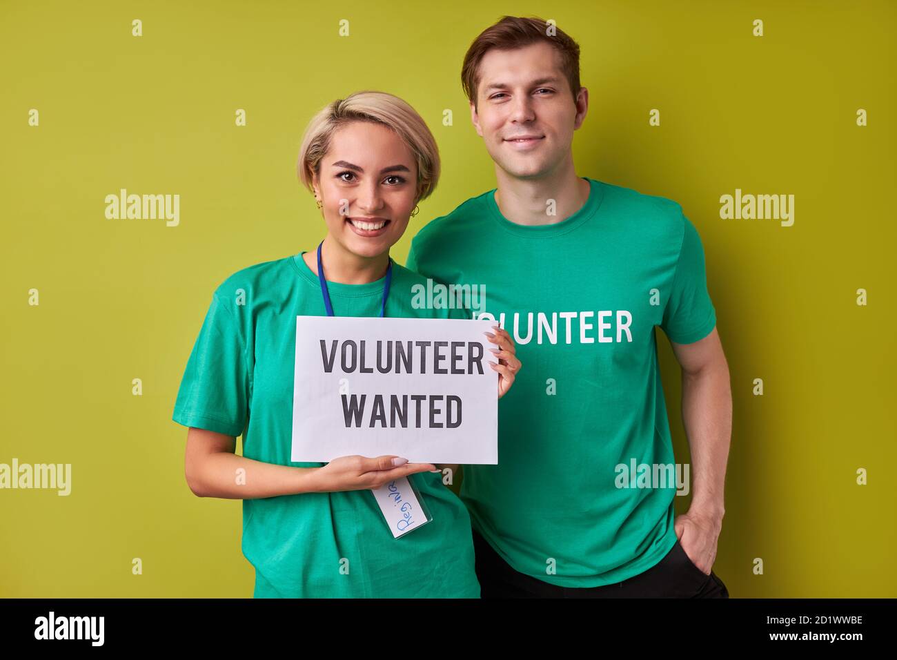 Zwei kaukasische Mann und Frau warten auf neue Menschen in ihrer Wohltätigkeitsorganisation, halten sie Papier mit Beschreibung Freiwilligen gesucht Stockfoto