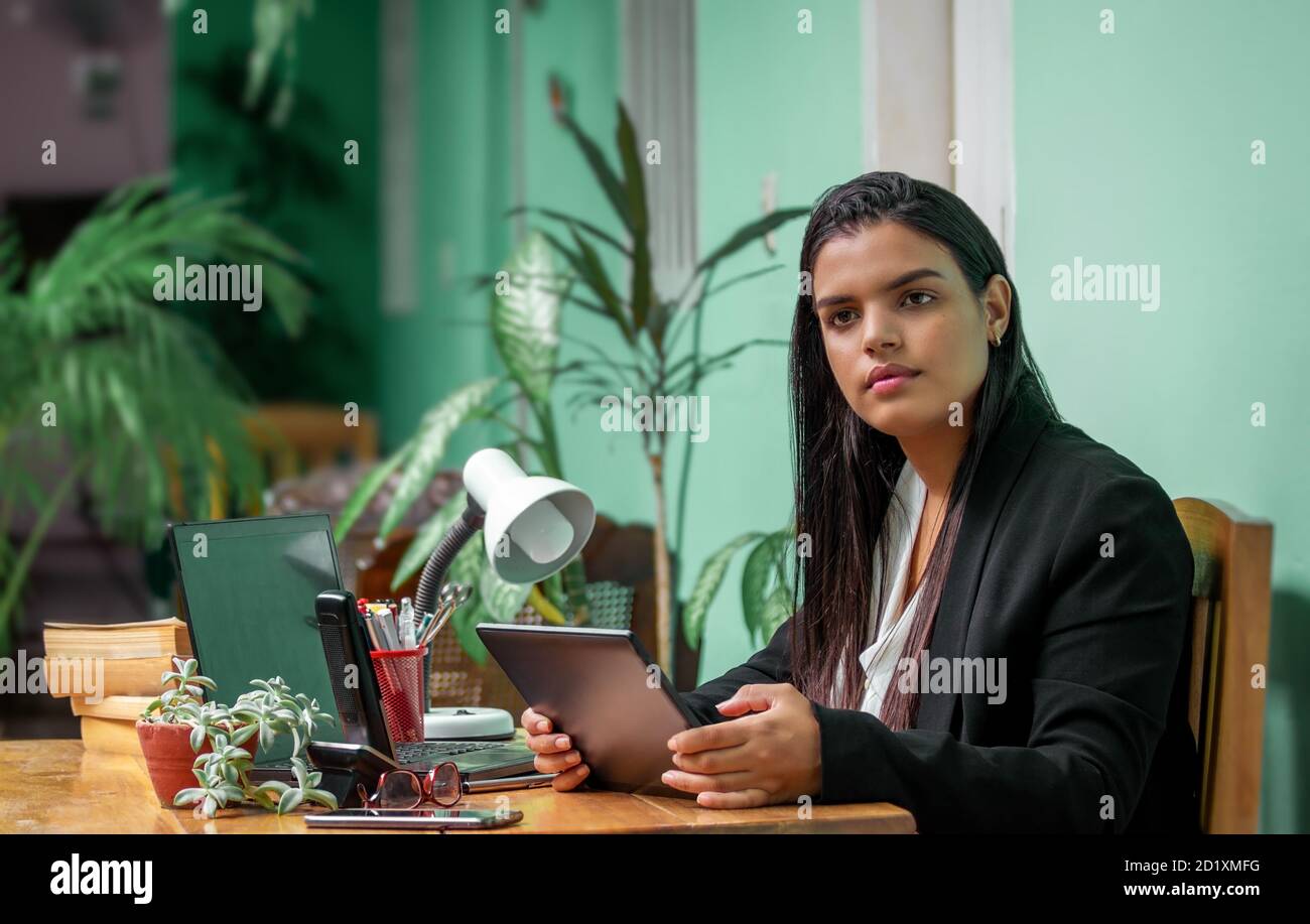 Junge Frau mit langen schwarzen Haaren sitzt an einem Schreibtisch mit einem Tablet in den Händen. Stockfoto