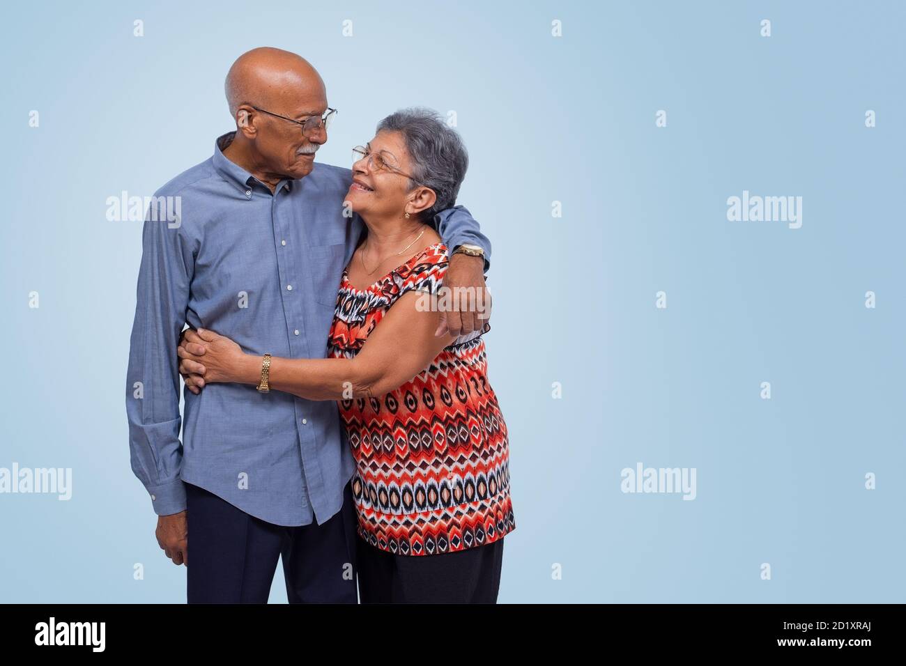 Ältere Paare stehen, umarmen und einander angucken. Hellblauer Verlaufshintergrund Stockfoto