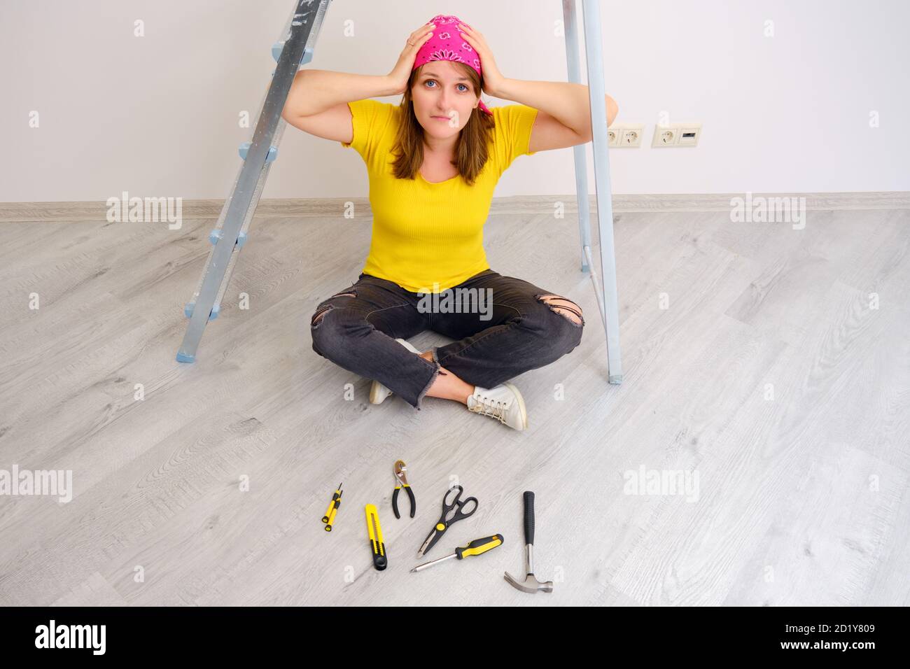 Eine Frau trauerte und traurig wegen der Sorgen, ein Haus mit ihren eigenen Händen zu reparieren. Er legte Bauwerkzeuge vor sich hin Stockfoto