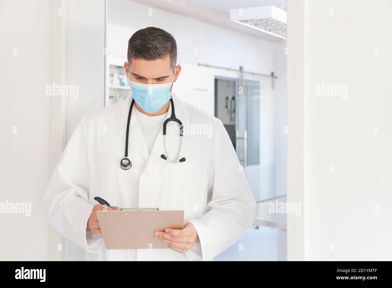 Junger Arzt mit OP-Maske vor der Operation nehmen Notizen - Fokus auf das Gesicht Stockfoto