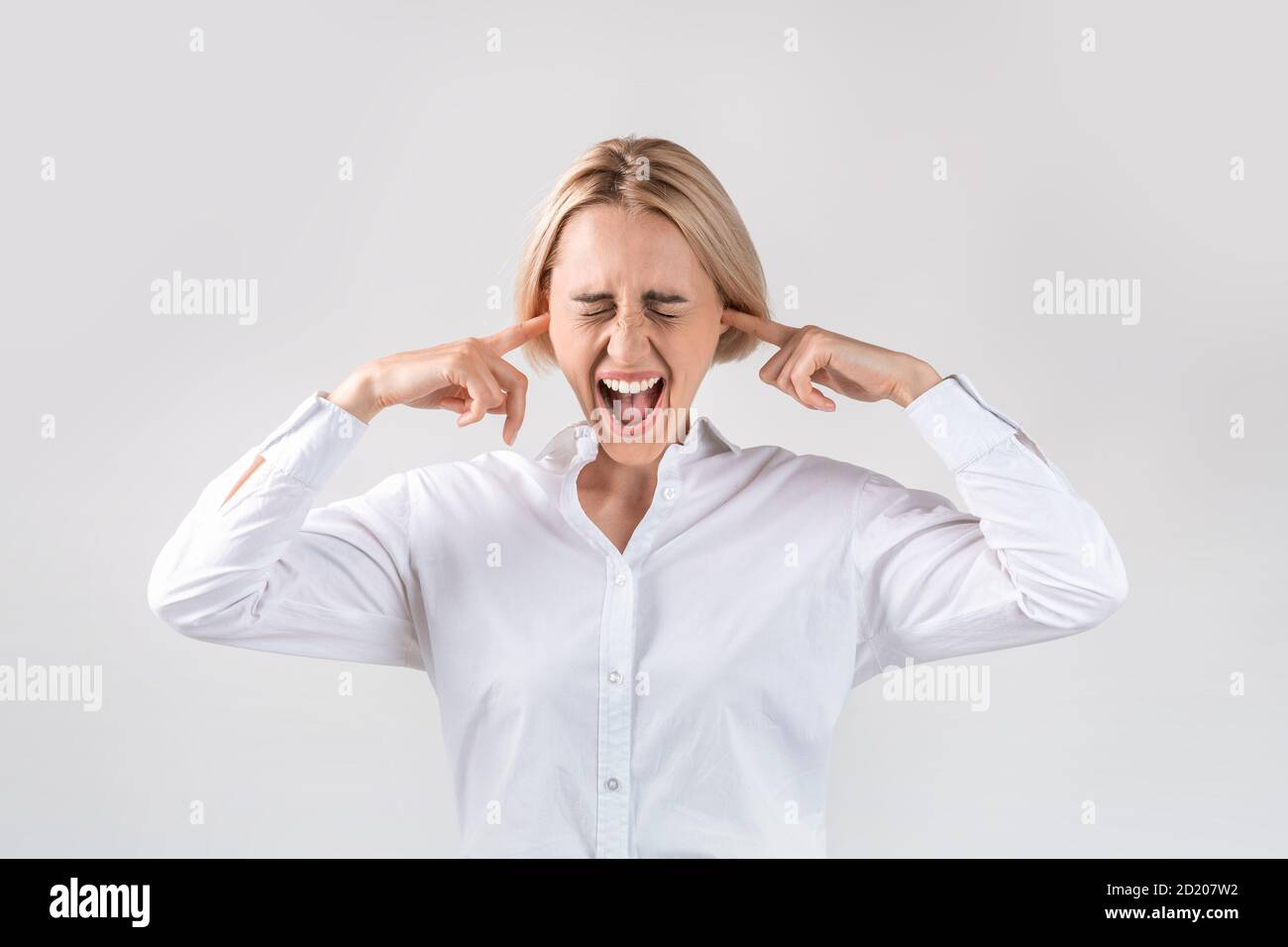 Attraktive Geschäftsfrau, die ihre Ohren schließt und vor Wut schreit Auf hellgrauem Studiohintergrund Stockfoto