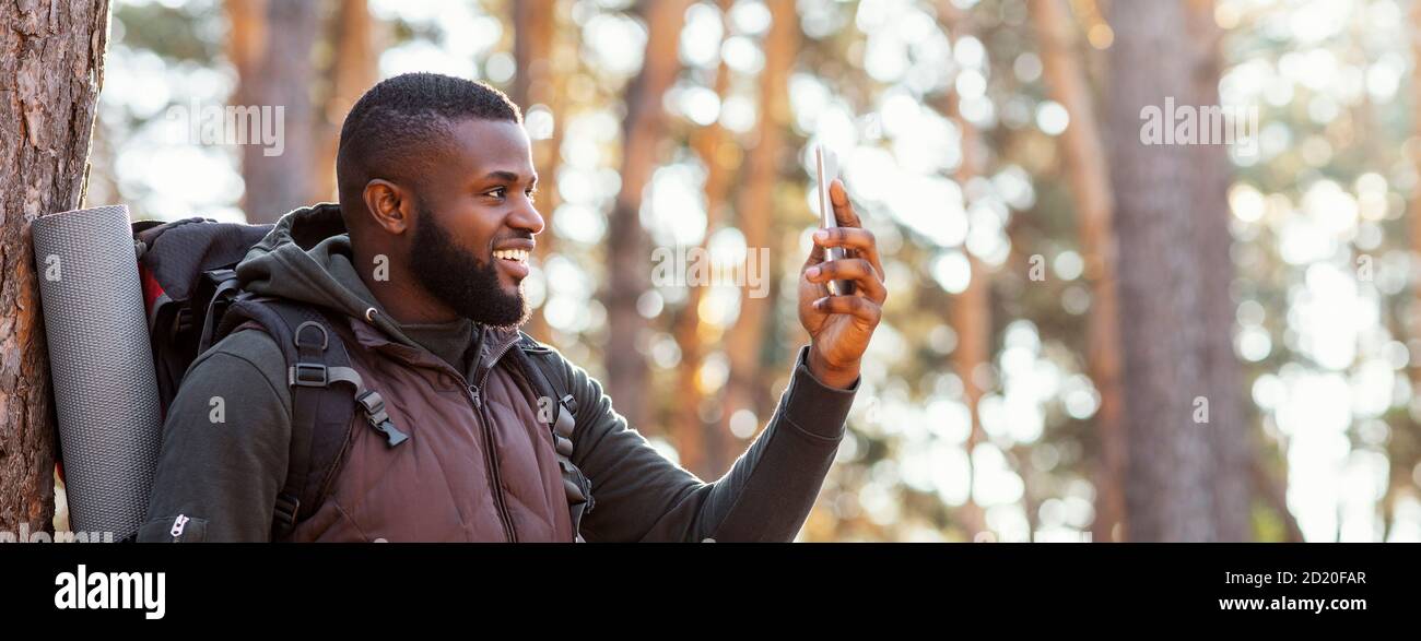 Afrikanischer Mann Backpacker mit Smartphone im Wald Stockfoto