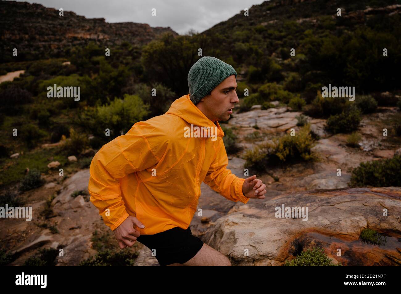 Müde fit Teenager männlich Sprinten auf felsigen Bergpfad in Nasses Wetter mit grünen Büschen und steilen Hügeln Stockfoto