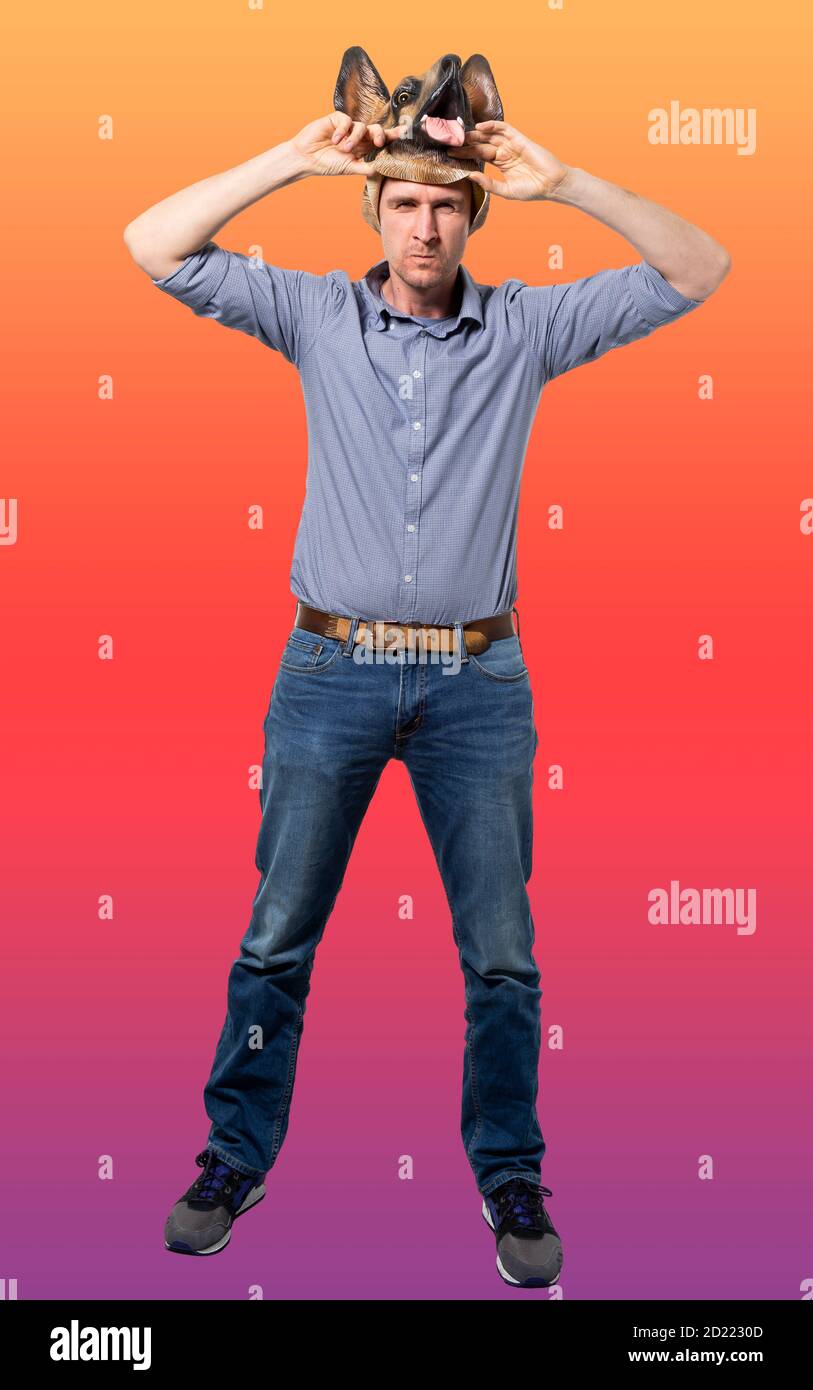 Kaukasischer Mann, der Hundemaske mit wütender Gesichtsausdruck auszieht. Volle Länge. Isolierter, farbenfroher Hintergrund. Studioaufnahme. Stockfoto