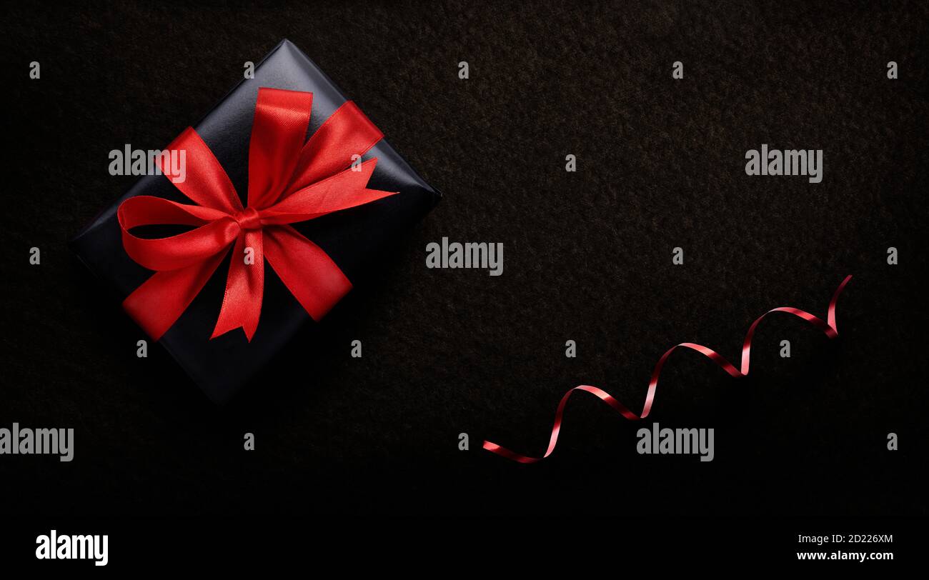 Ein Geschenk zum Geburtstag, Weihnachten oder Valentinstag, in schwarzem Papier und rotem Band auf dunklem Hintergrund von oben verpackt. Stockfoto