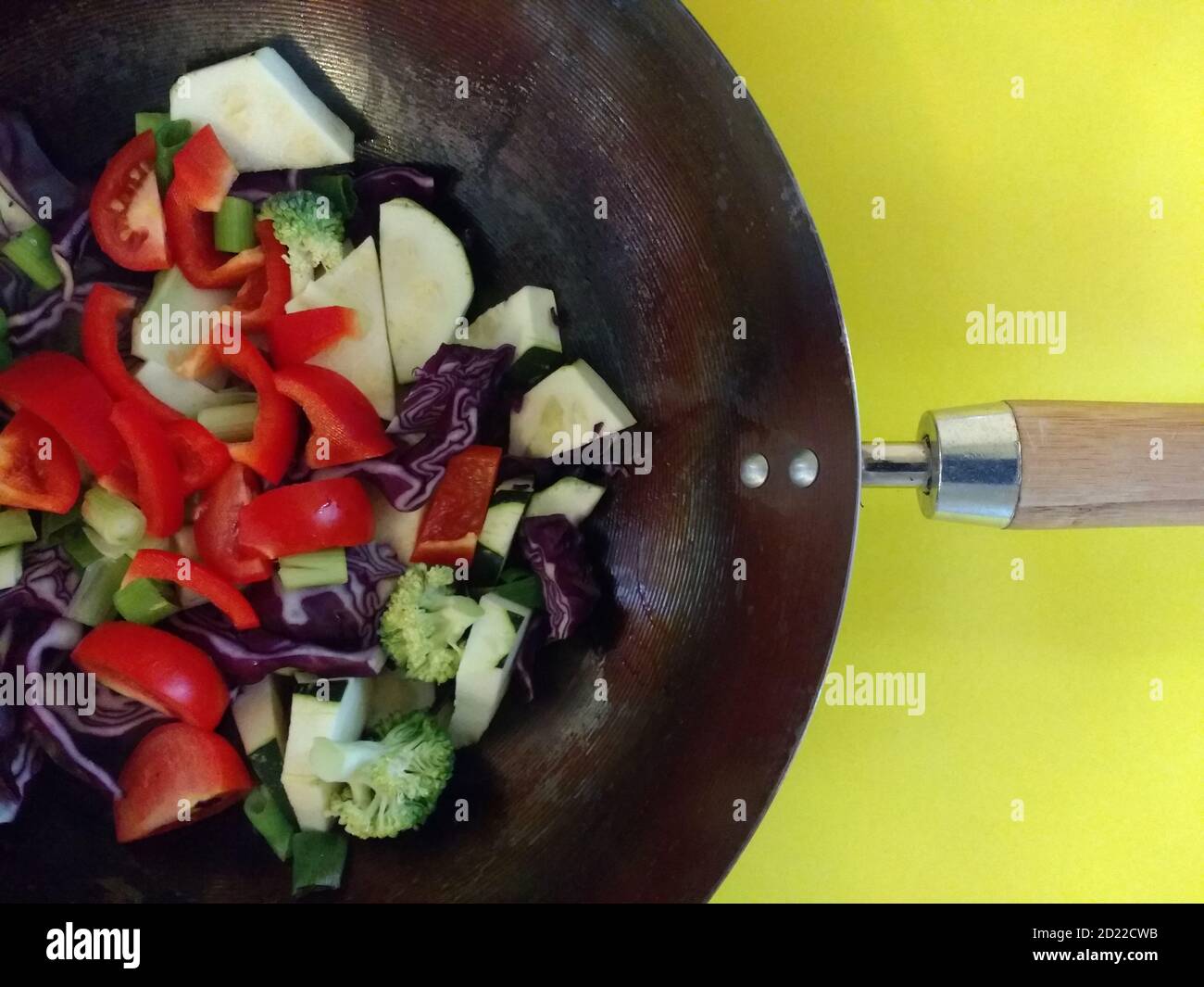 Nahaufnahme von veganen Rührbraten Mahlzeit Bio frischen Garten Gemüse von Tomaten, Brokkoli, Pfeffer, Kohl gekochtes Kokosöl in Metall Wok gelben Hintergrund Stockfoto