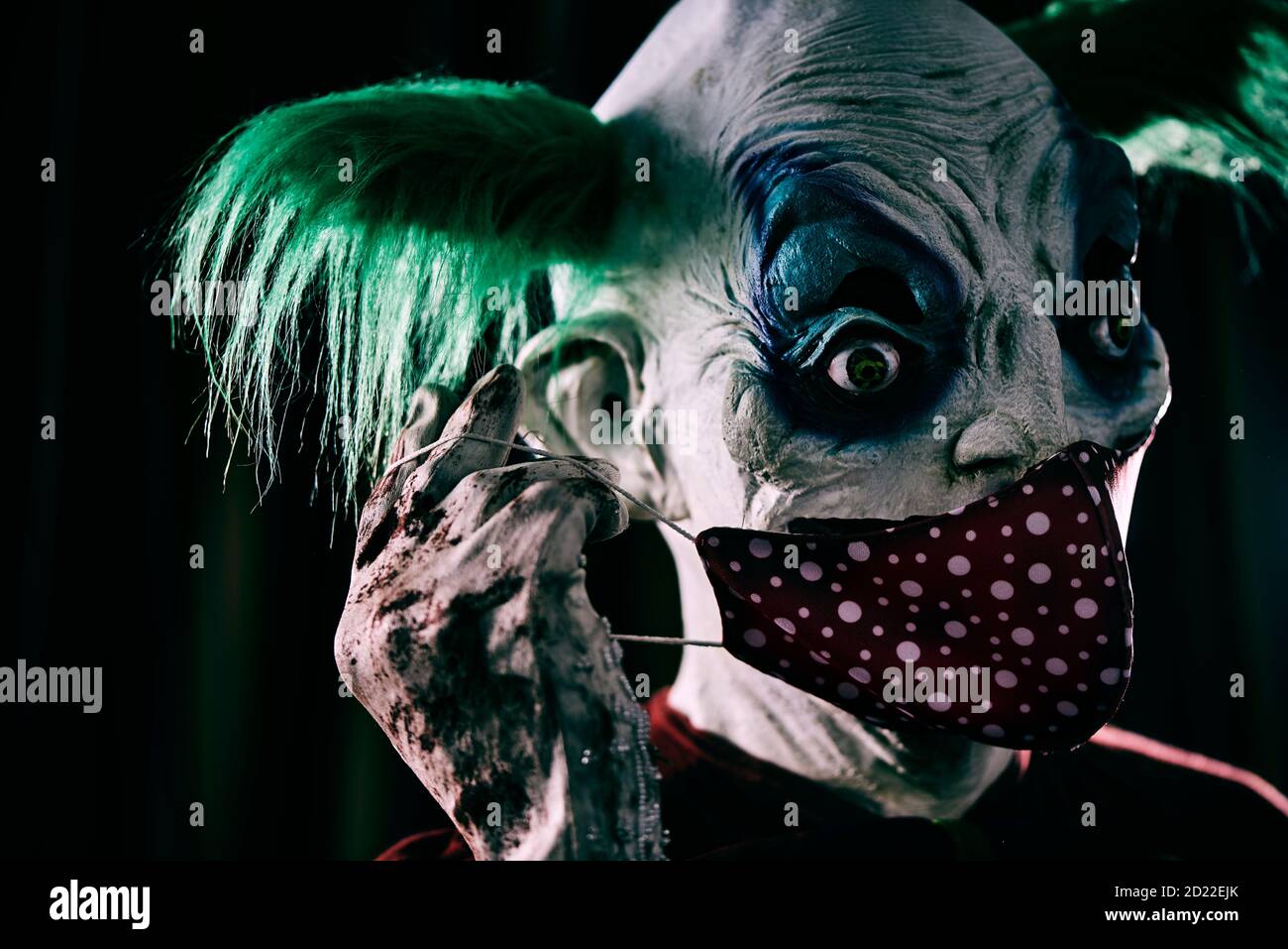 Nahaufnahme eines verstörenden bösen Clowns, mit grünen Haaren, trägt ein schmutziges rotes Kostüm, eine schmutzige Fliege, und schmutzige und blutige Handschuhe, ziehen sein rotes Gesicht m Stockfoto