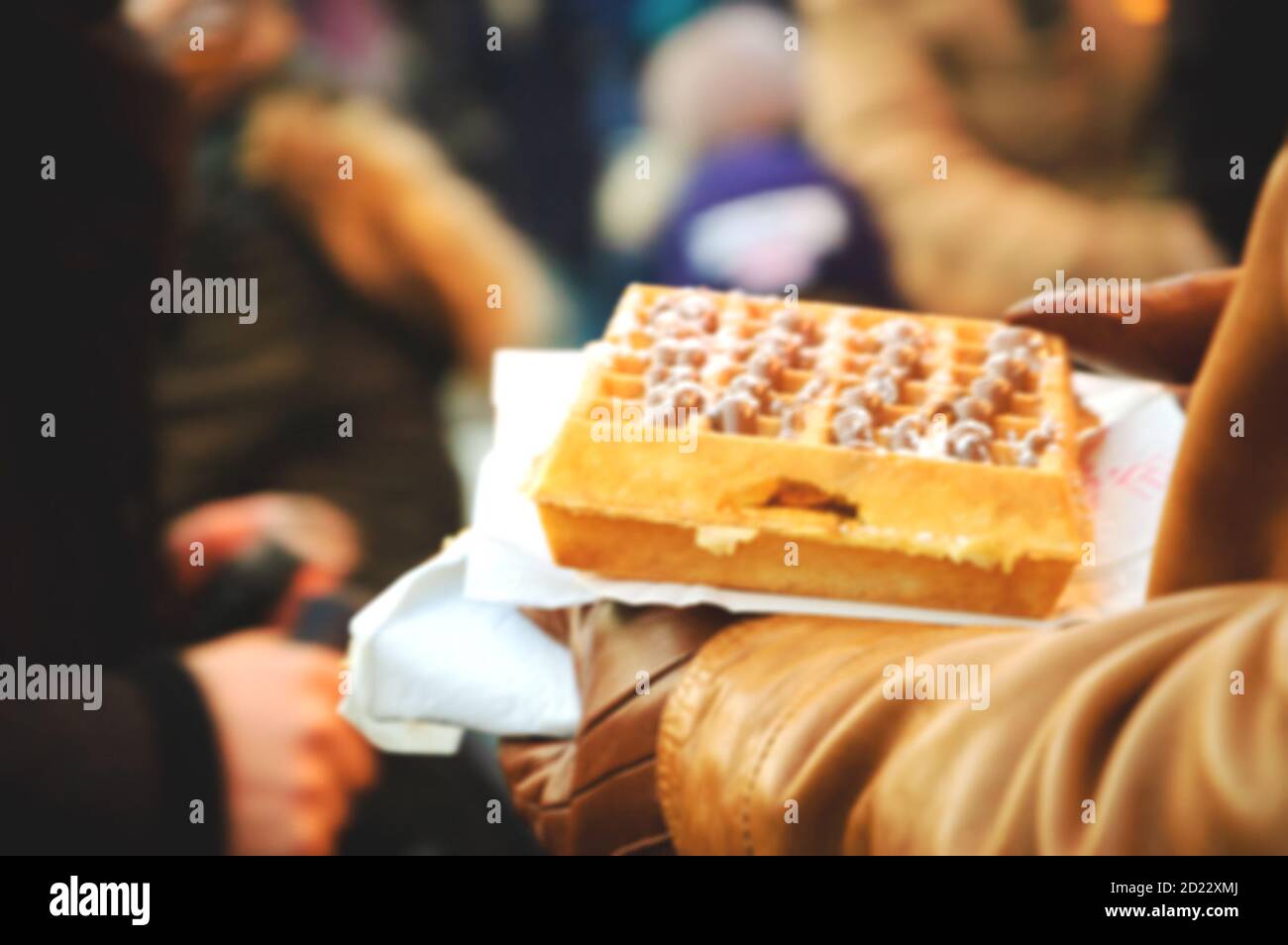 Verschwommenes Foto eines Mannes, der vorsichtig eine belgische Waffel in der Menge des Weihnachtsmarktes trägt. Paris (Frankreich). Stockfoto