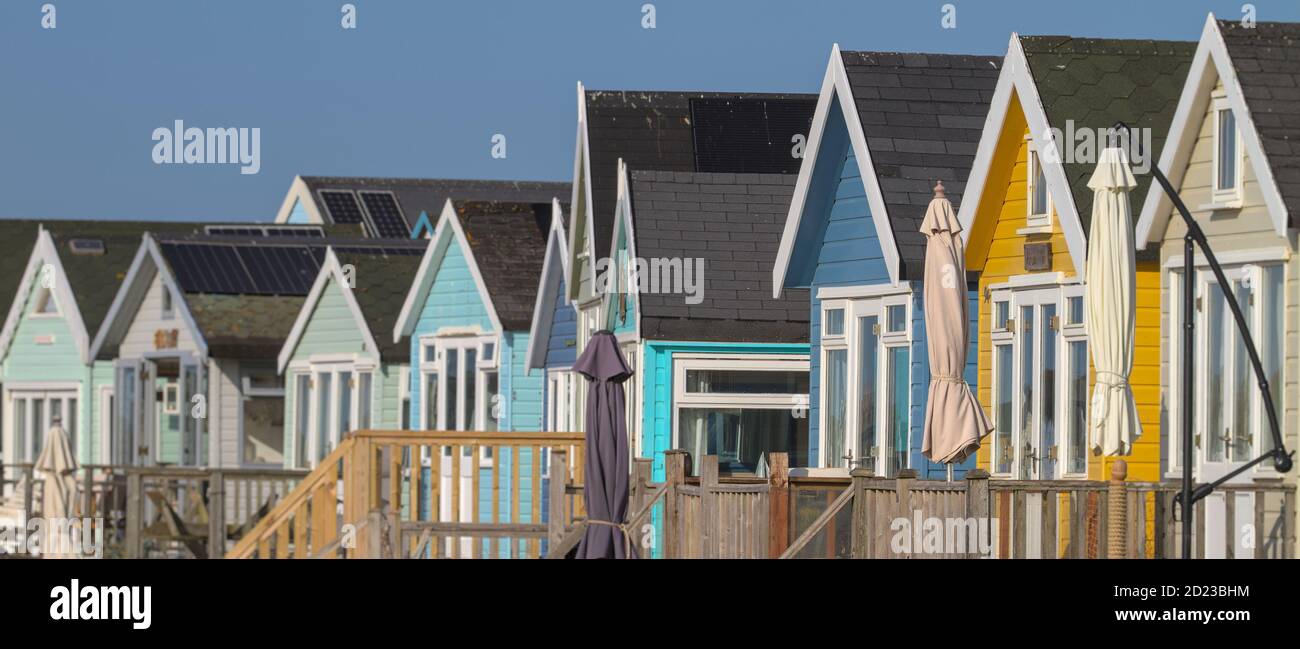 Reihe Von Bunten Hölzernen Strandhütten Mit Sonnenschirmen. Aufgenommen in Mudeford Sandspit UK Stockfoto