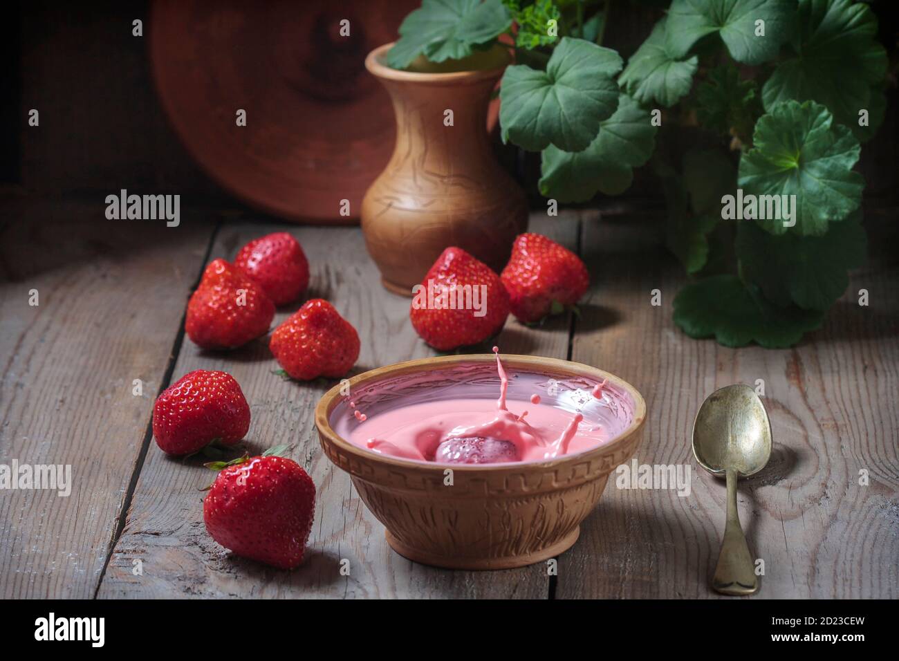 Milchdessert mit Erdbeeren in einer Keramikschale auf Holzgrund. Herabfallende Erdbeeren und Milchspritzer, Joghurt. Stockfoto