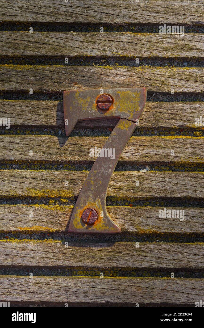 Alt, alt, verwittert gebrochenes Messing Nummer sieben auf EINER Holzterasche verschraubt. Aufgenommen in Mudeford UK Stockfoto