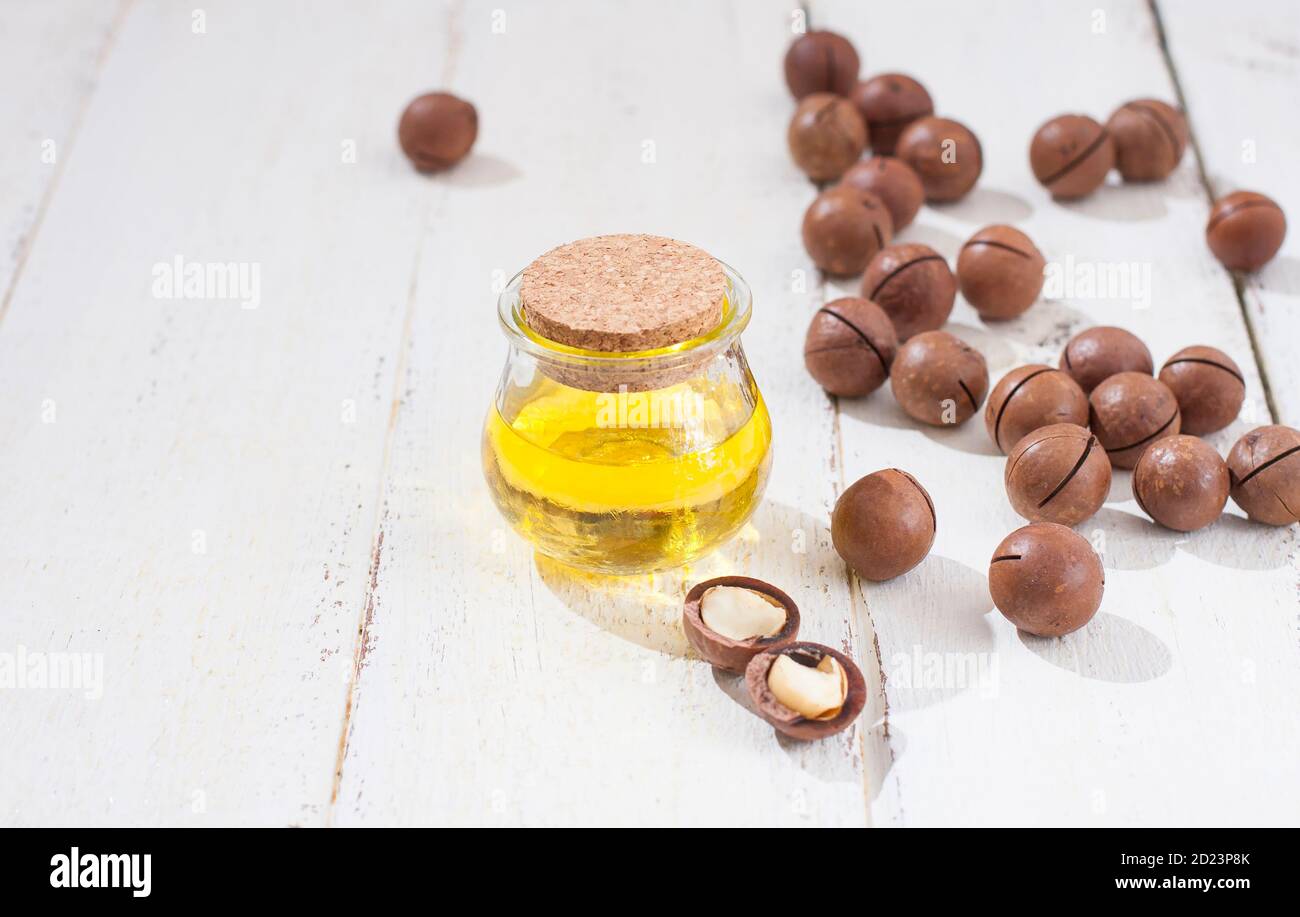 Natürliches Macadamiaöl und Macadamianüsse auf weißem Holzbrett. Gesundes Produkt. Gesunde Ernährung Konzept. Stockfoto