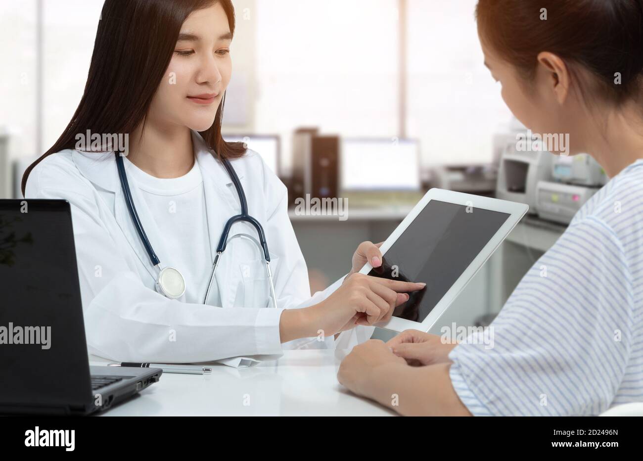 Asiatische Frau Arzt hält Tablette mit isolierten leeren Bildschirm, während die Beratung Patient in der medizinischen Beratungsraum. Stockfoto