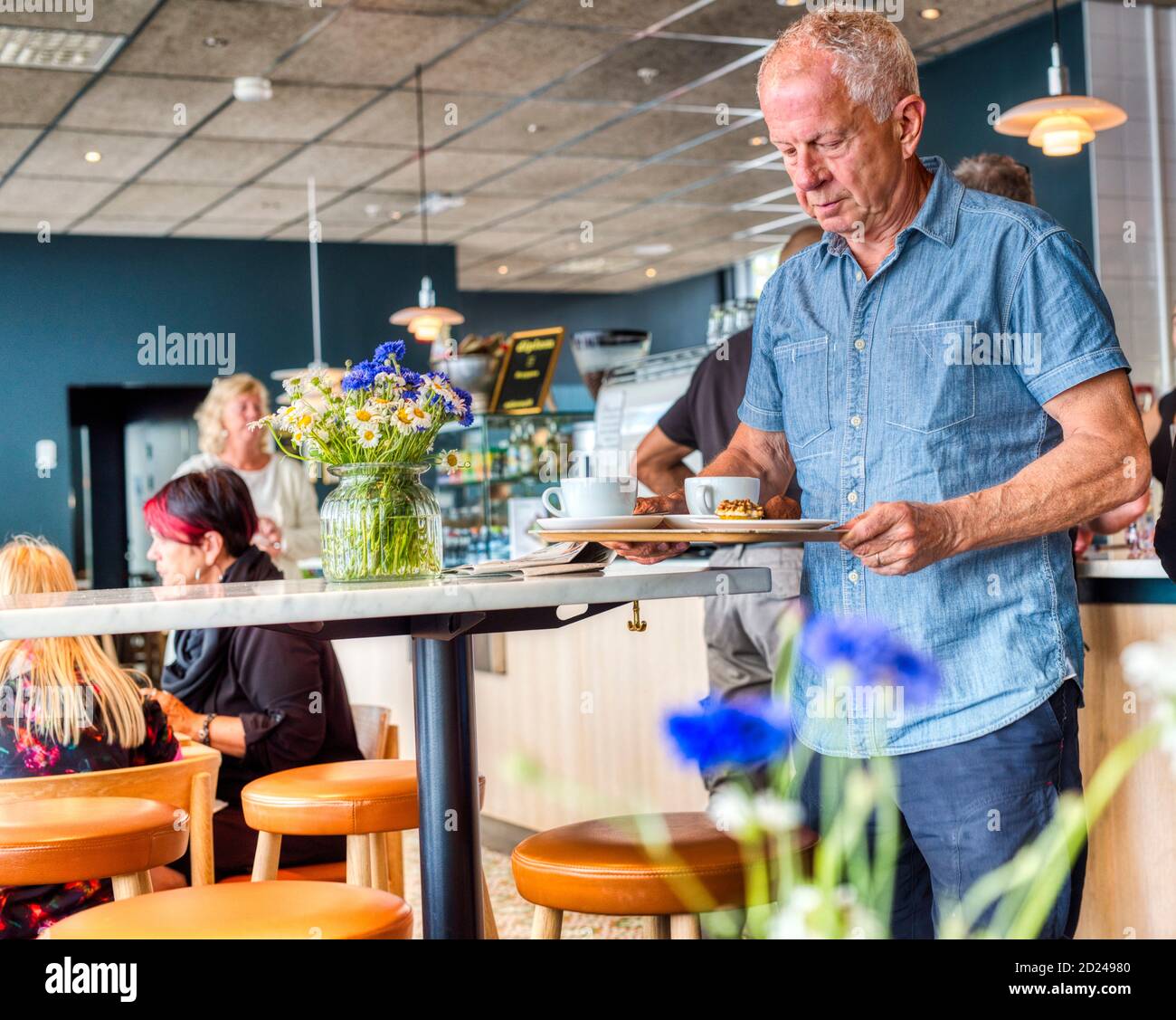 Ein älterer Mann, der sein Tablett in einem Café trägt Stockfoto