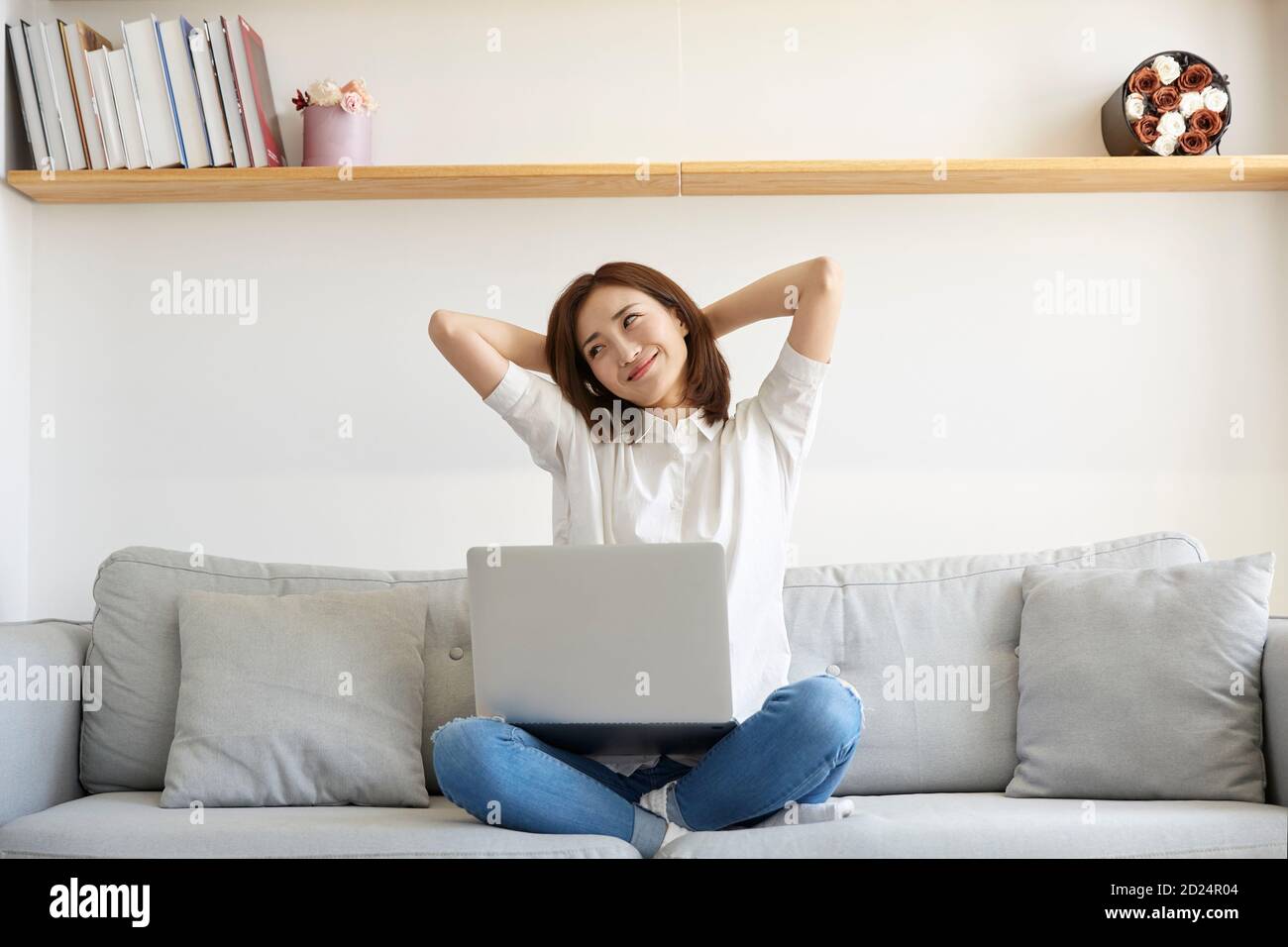 Junge asiatische Geschäftsfrau, die von zu Hause aus auf der Couch sitzt Streckt die Arme glücklich und lächelnd Stockfoto
