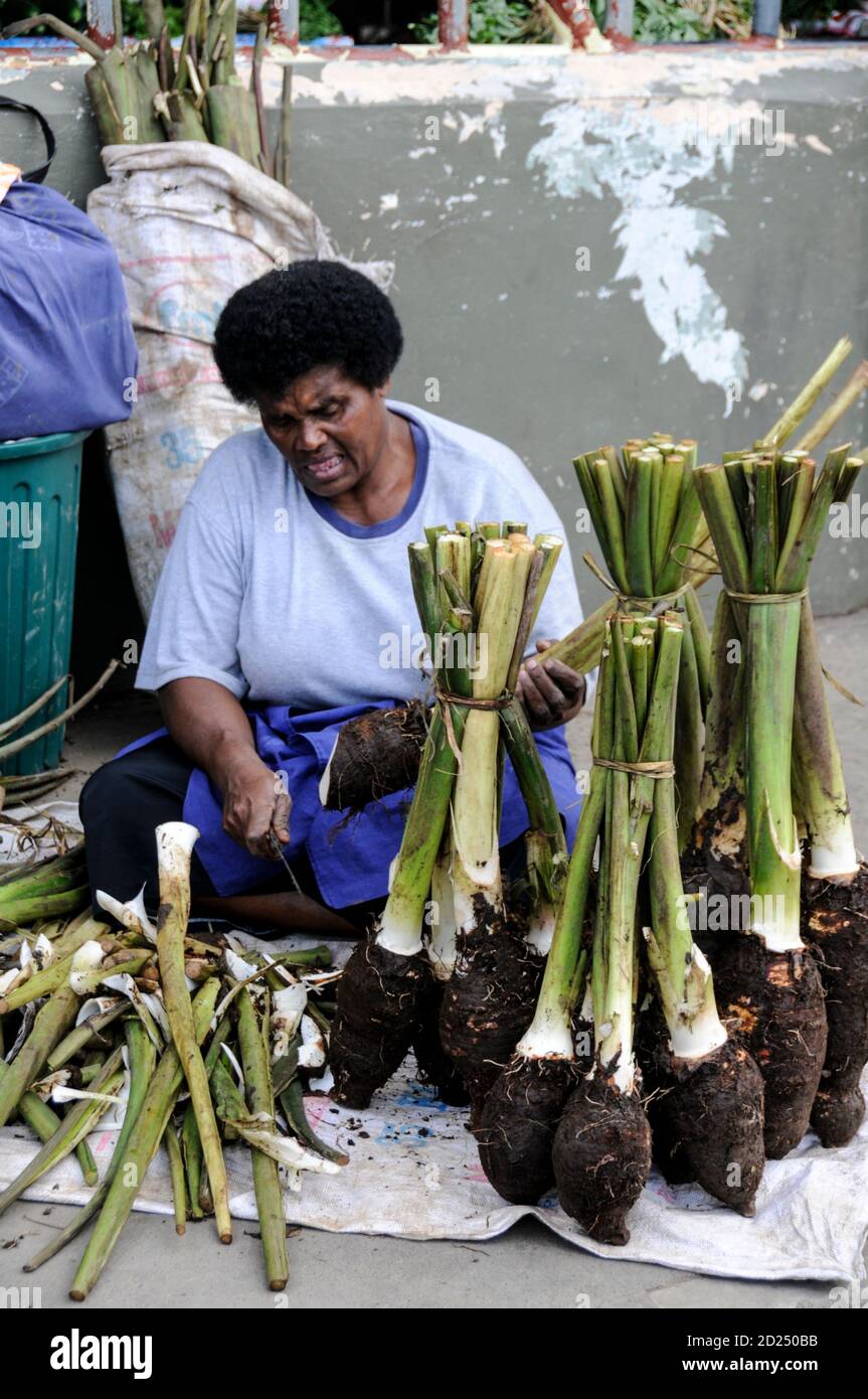 Eine Frau hackt einen Haufen Fidschi Dalo auf einem lokal produzierten Obst  & Gemse Markt in Sigatoka auf Viti Levu, Fidschi. Der Dalo ist eine  Wurzelpflanze und wird gekocht Stockfotografie - Alamy