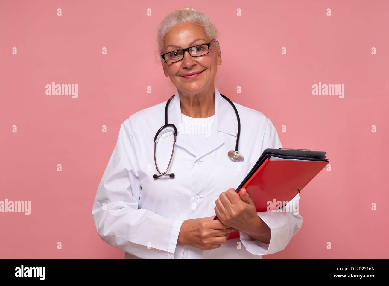 Ältere Ärztin mit Ordnern, die mit einem Lächeln auf die Kamera schauen. Stockfoto