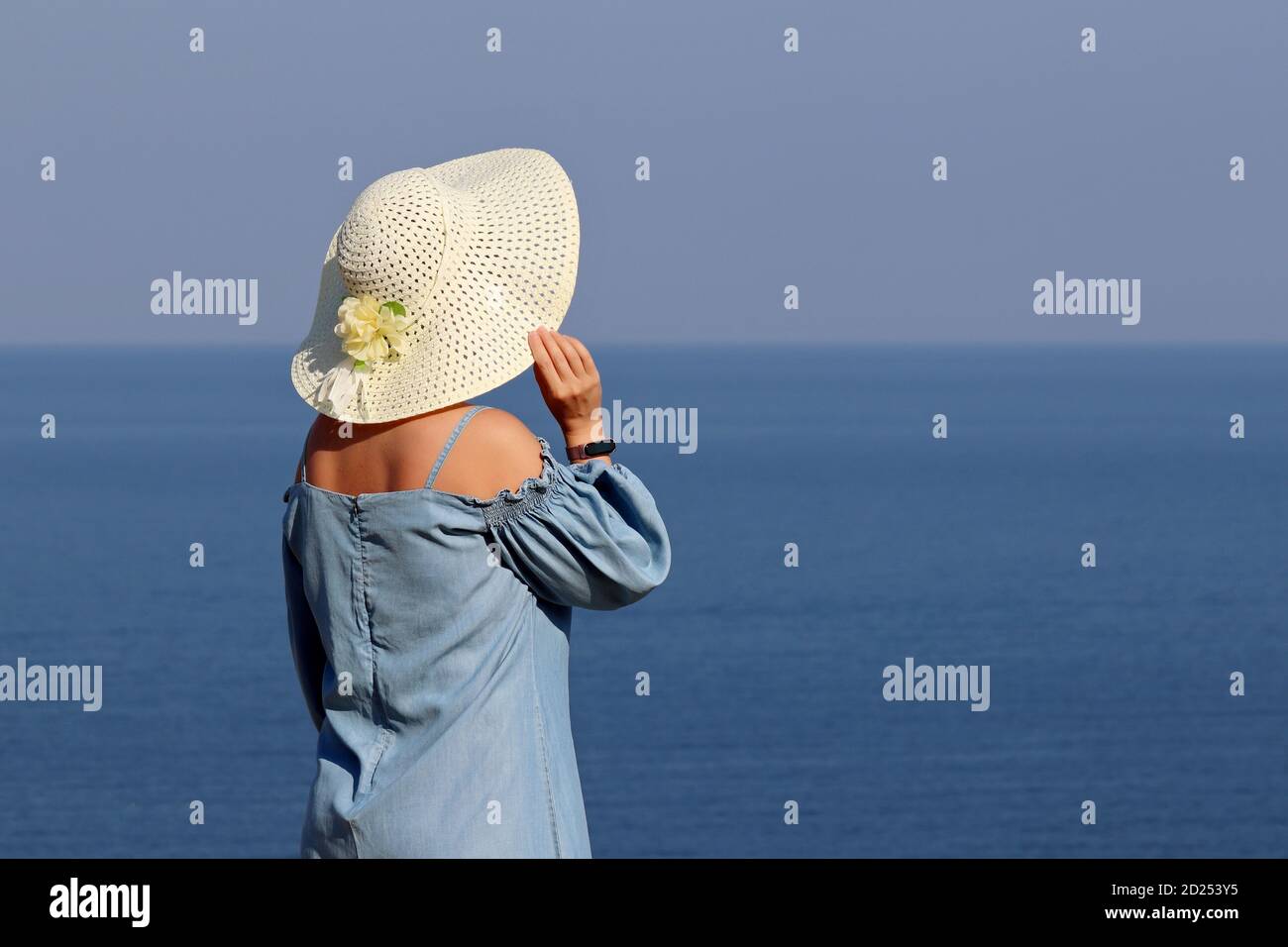 Frau in Sonnenhut und blauem Kleid auf einem Meer Hintergrund stehen. Strandurlaub, entspannen und träumen Konzept Stockfoto