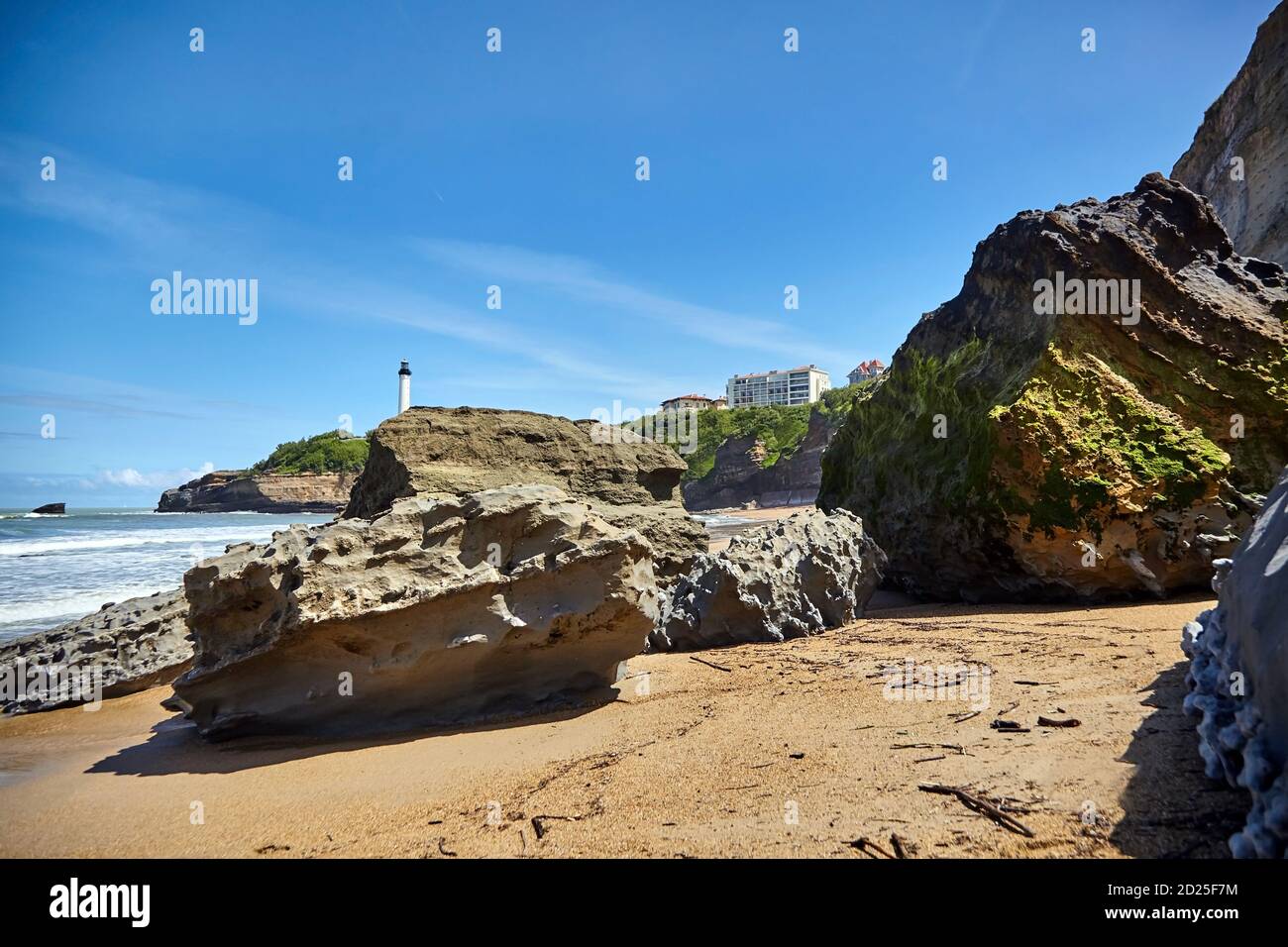 Riesige Felsbrocken am Sandstrand Miramar Plage mit Blick auf den weißen Leuchtturm - Phare de Biarritz an der Pointe Saint-Martin. Bucht von Biskaya, Atlanti Stockfoto