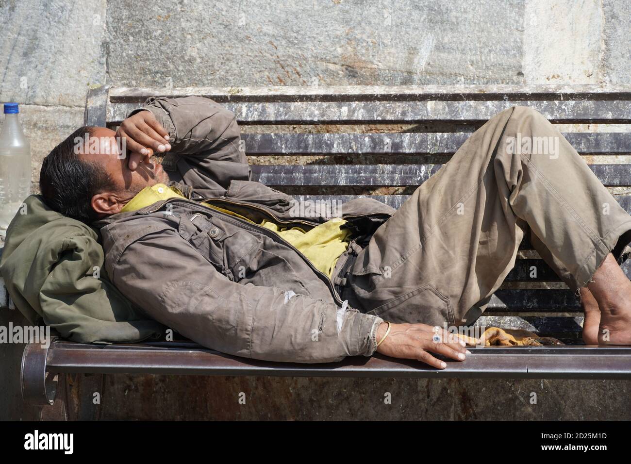 Armer obdachloser Bettler oder Flüchtling, der tagsüber auf einer schmutzigen Holzbank in einer Einbahnstraße in der Stadt schläft. Sozialdokumentarisches Konzept. Schuh Stockfoto