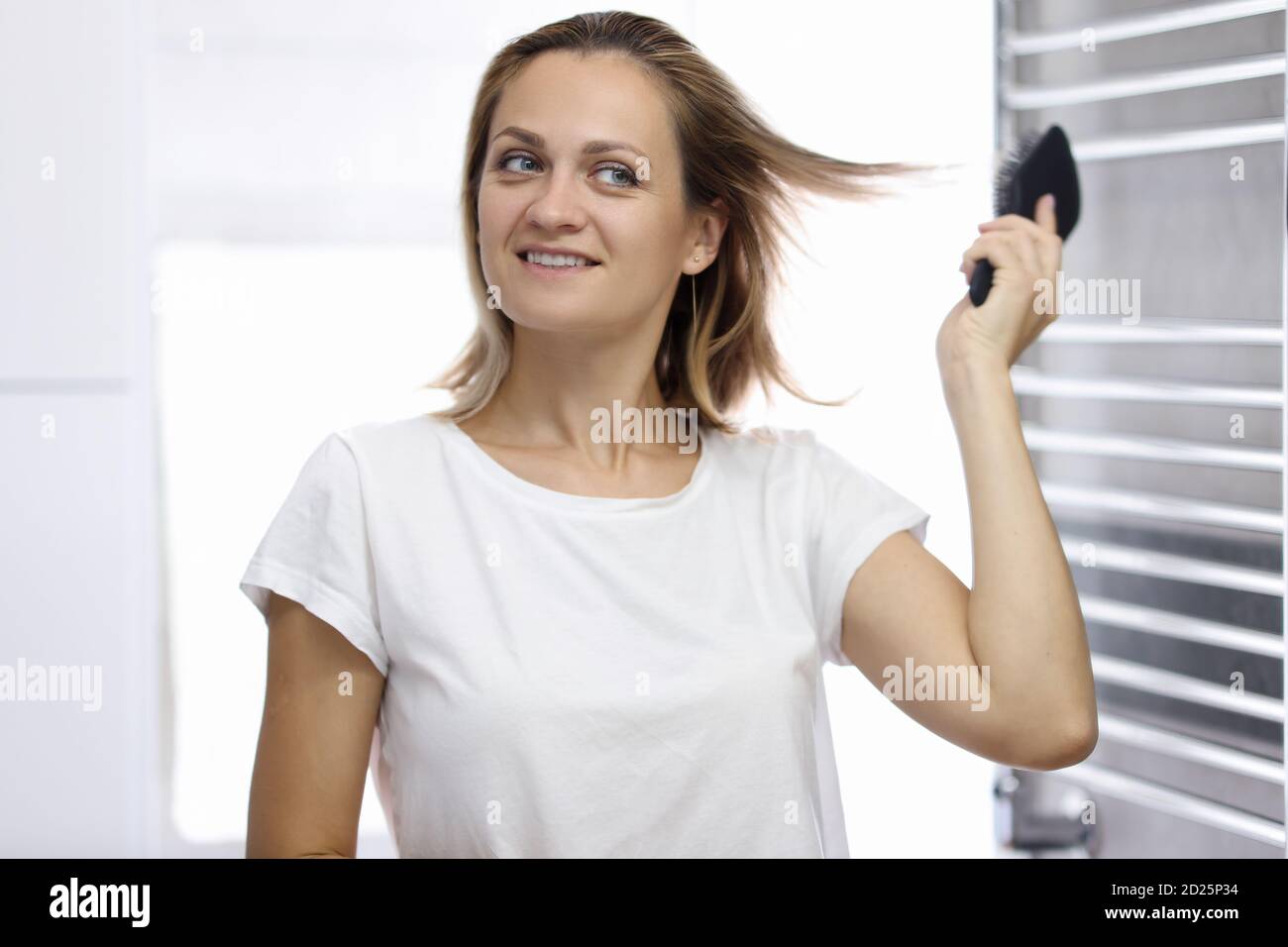 Junge schöne Frau schaut auf ihre Reflexion im Badezimmer Und kämmen ihr Haar Stockfoto