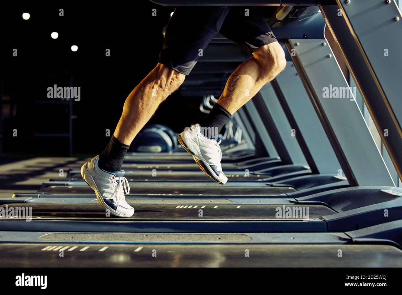 Kurze Aufnahme eines sportlichen Mannes in Sportbekleidung, der auf einem Laufband in einem Fitnessstudio läuft, konzentrieren Sie sich auf die Beine Stockfoto