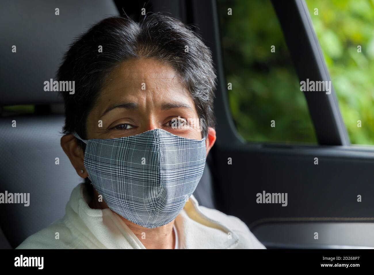Britische asiatische Frau (BAME) trägt Gesichtsmaske in einem Auto. COVID oder Coronavirus-Konzept, Prävention und Selbstisolierung in Großbritannien. Stockfoto