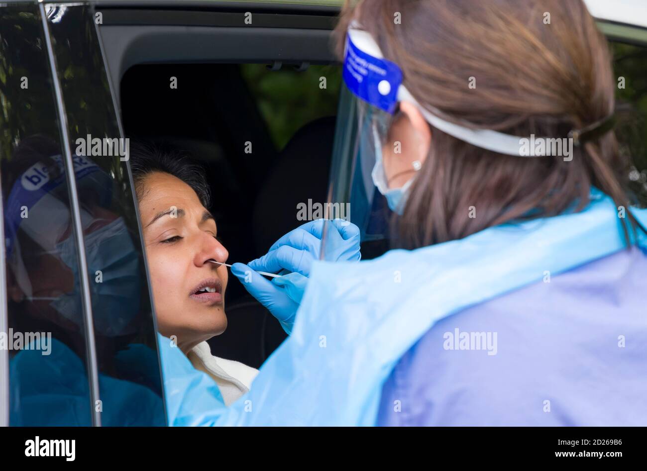 Asiatische Frau in einem Auto mit einem Coronavirus Nasenabstrich Test mit einer Krankenschwester in PSA-Ausrüstung. England, Großbritannien Stockfoto