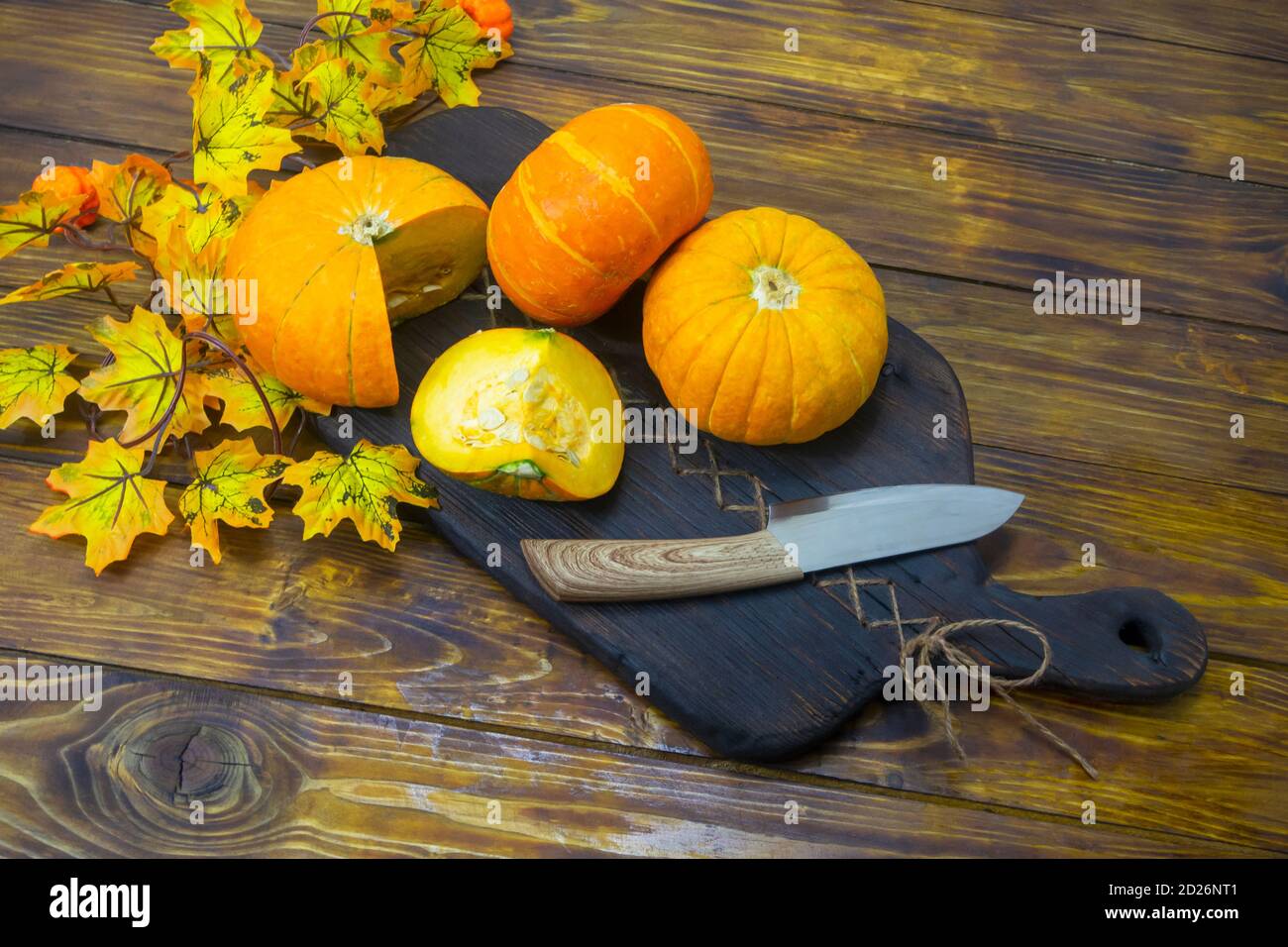 Stillleben im Herbst auf dunklem Holzgrund. Kleine gelbe Kürbisse und Messer. Konzept der Öko-Produkte, Herbsternte von Gemüse. Dunkler Hintergrund, Stockfoto