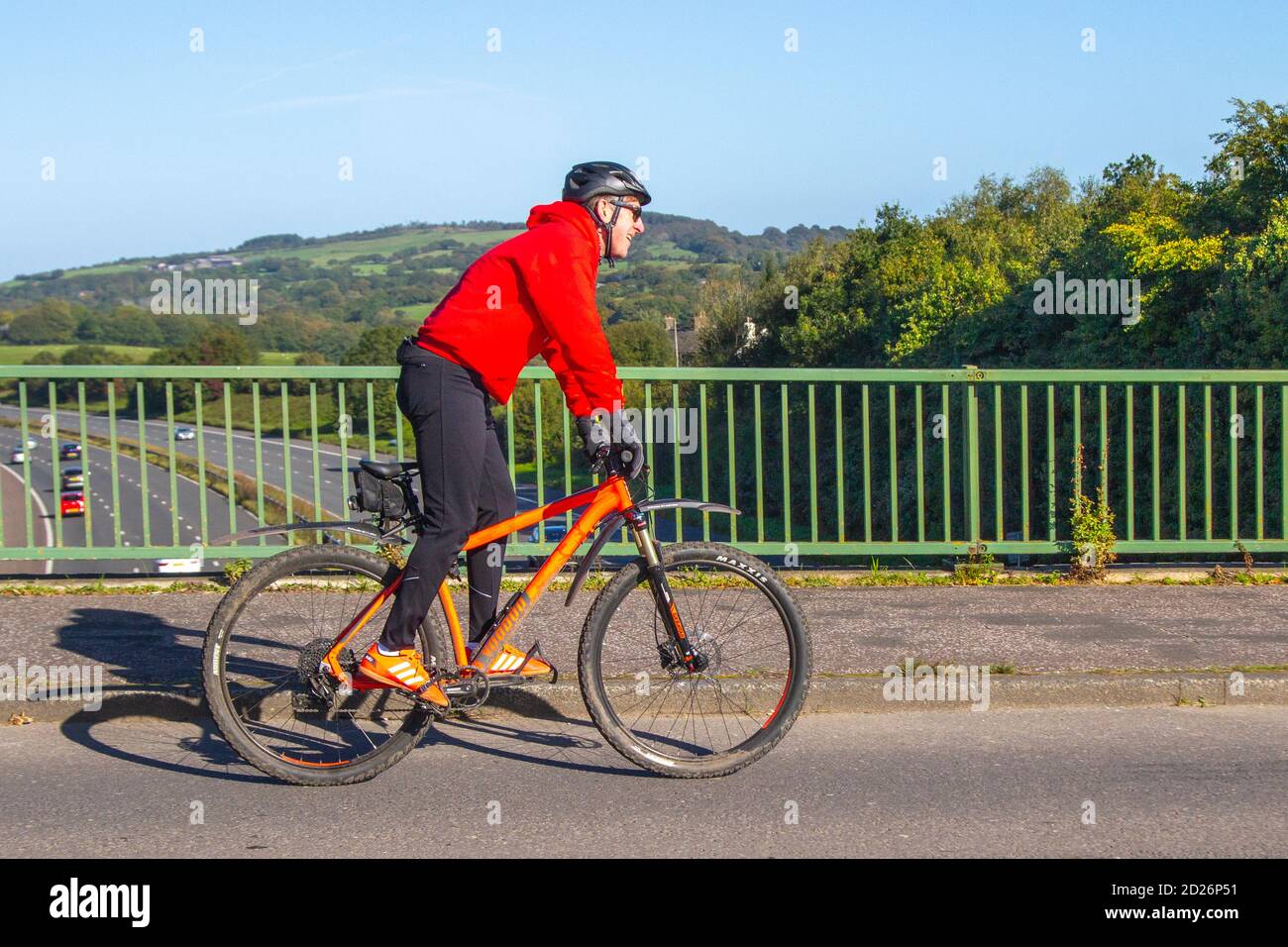 Männlicher Radfahrer Reiten Voodoo orange Sport Mountainbike auf dem Land Route Überqueren Autobahnbrücke im ländlichen Lancashire, Großbritannien Stockfoto