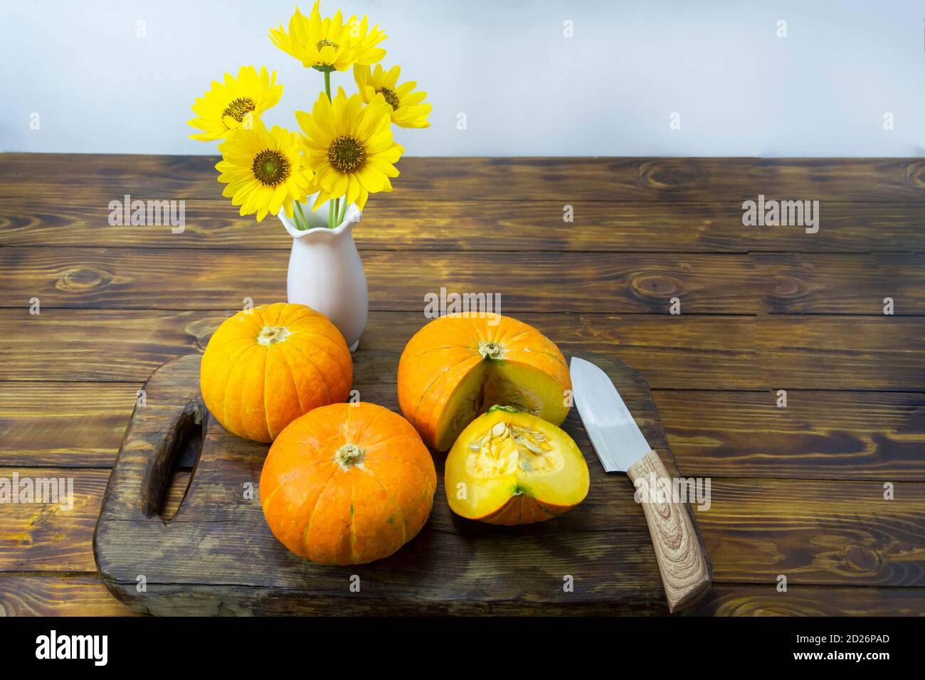 Kürbisse auf dunklem Holztisch und Messer. Schöne gelbe Blumen in Vase. Stillleben im Herbst. Konzept der Öko-Produkte, Herbsternte von Gemüse. Stockfoto