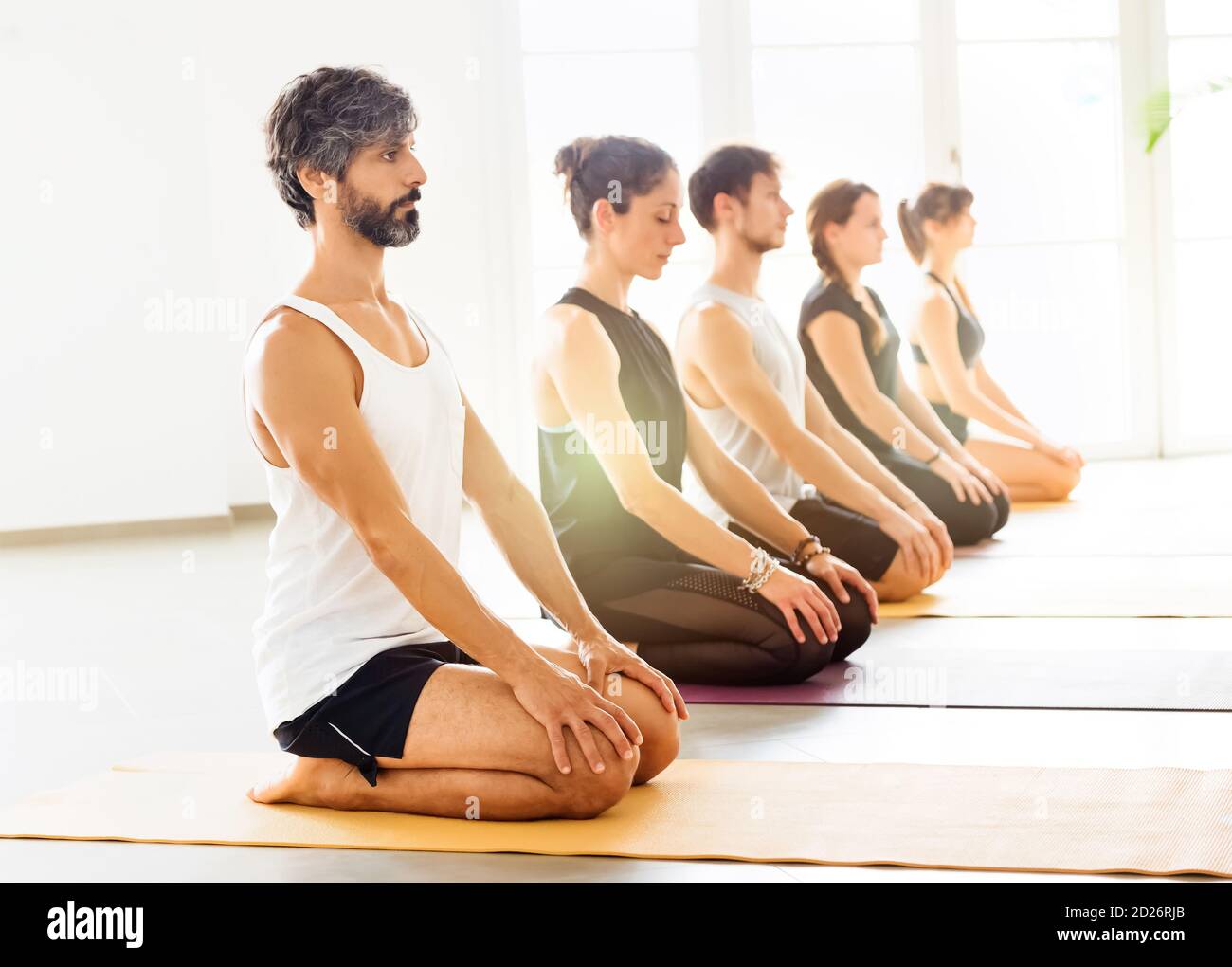 Reihe von Menschen während der Yoga-Klasse meditieren in Virasana Yoga Pose. Seitenansicht vor hellem Hintergrund in geräumigen Zimmer Stockfoto
