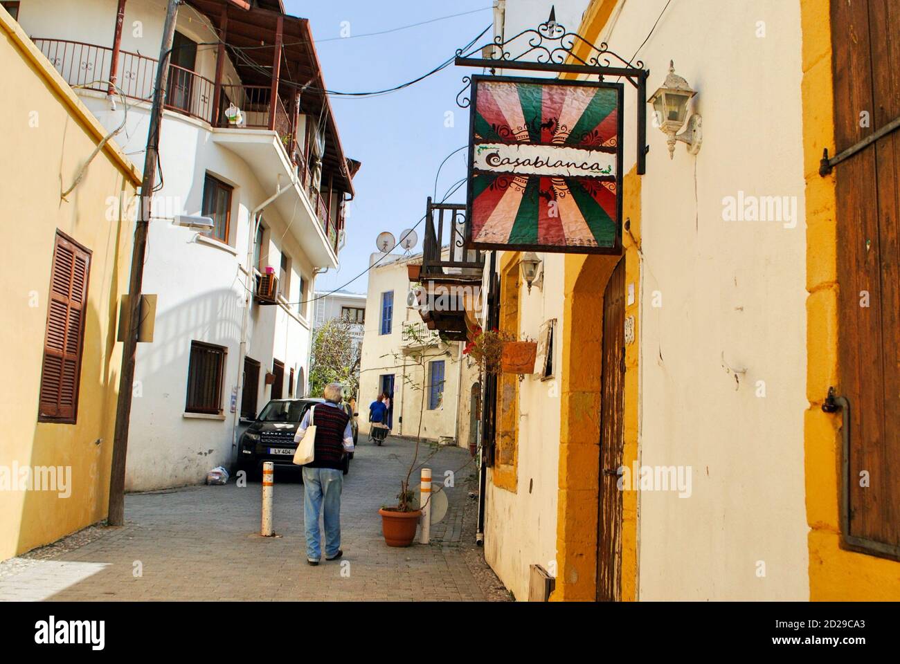 Girne, Kyrenia, Nordzypern. Ca. Mai 2019. Aktiver reifer männlicher Tourist, der an einem sonnigen Tag in einer engen Straße mit Cafés spazierengeht. Stockfoto