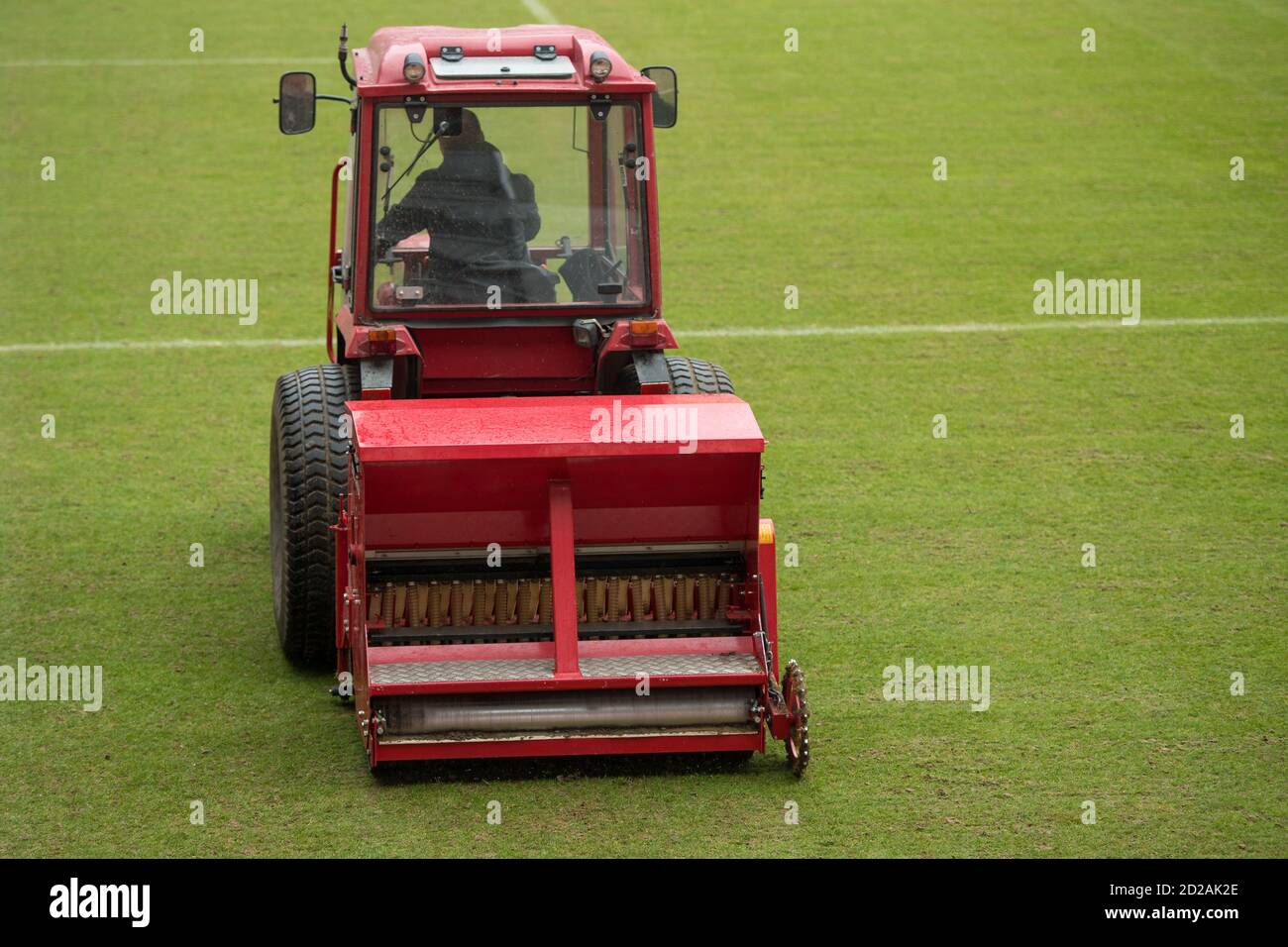 Ein Mann in einem Traktor mit einer Scheibensämaschine bohren Gras auf einem Fußballfeld gesäht Stockfoto