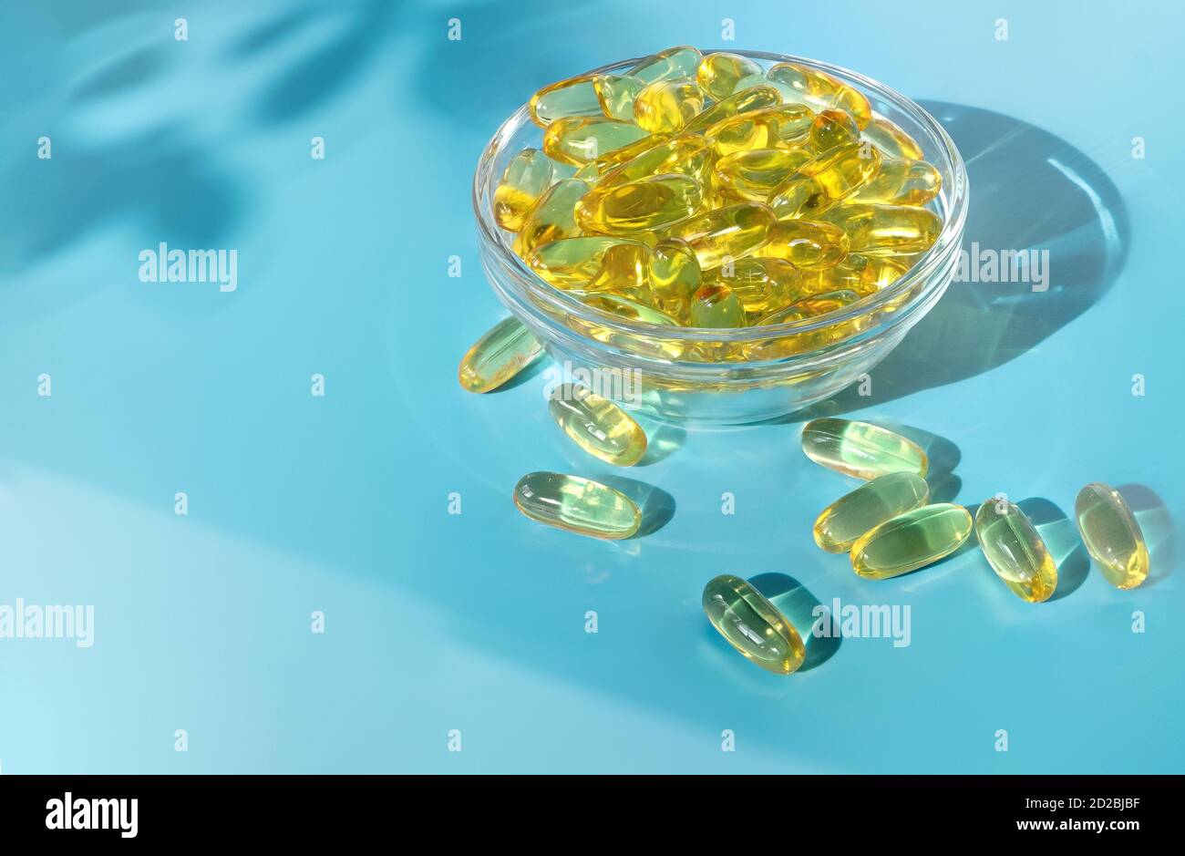 Gelatine transparente Kapseln mit Fischöl in einer Glasschüssel auf blauem Hintergrund. Stockfoto