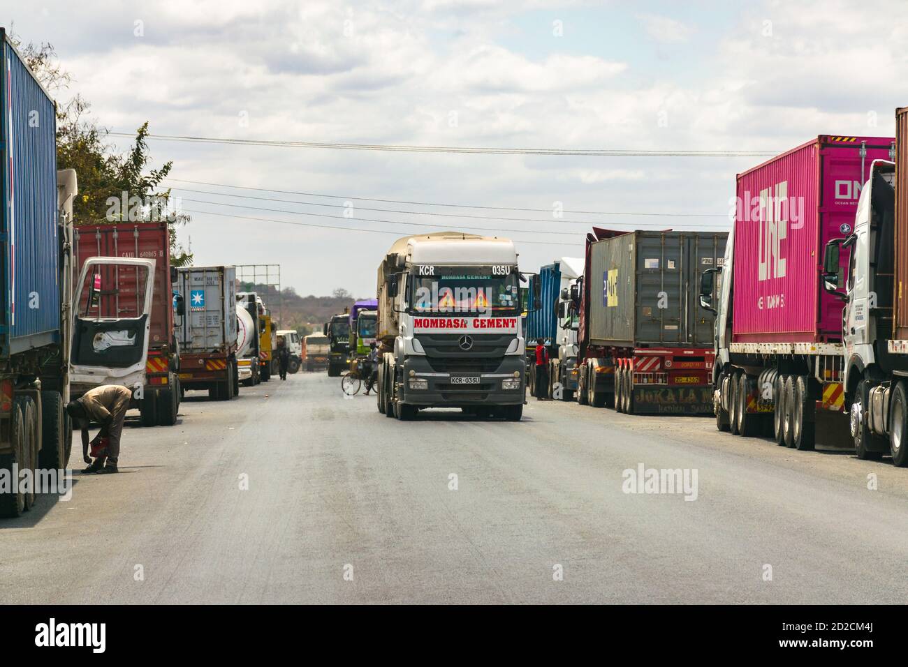 Reihen von großen LKWs oder LKWs säumen die Seite der Mombasa Autobahn, während andere LKWs vorbeifahren, Kenia, Ostafrika Stockfoto