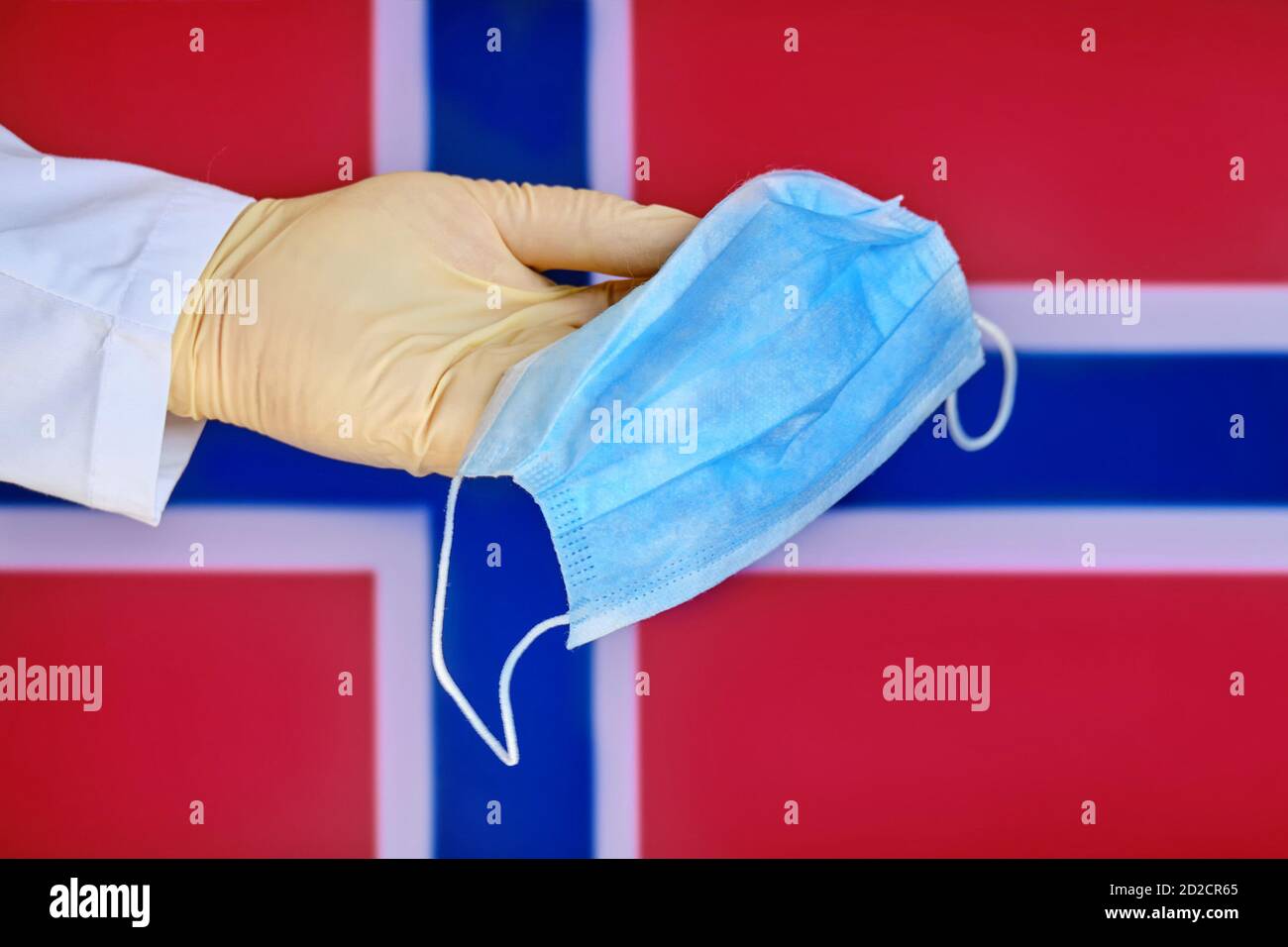 Medizinische Maske in den Händen eines Arztes und der Norwegen-Flagge, Kopierraum. Schutzhandschuh mit Maske Nahaufnahme auf dem Hintergrund des Staates Norwegian sy Stockfoto