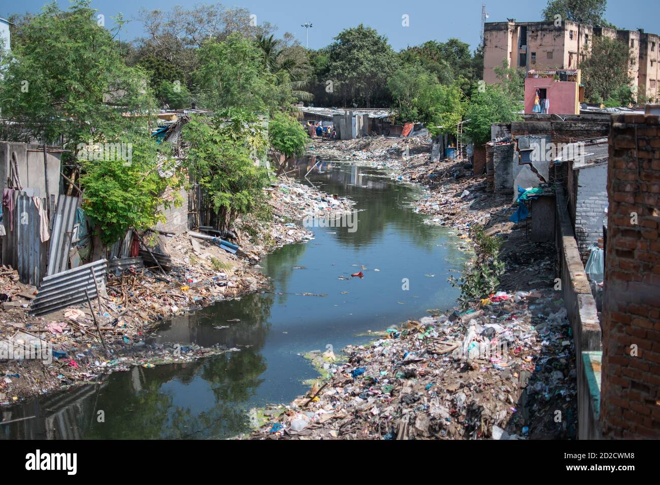 Ein Fluss gefüllt mit Plastikmüll Entsorgung umgeben von Gebäuden und Bäumen in den Slums von Chennai, Tamil Nadu, Indien Stockfoto