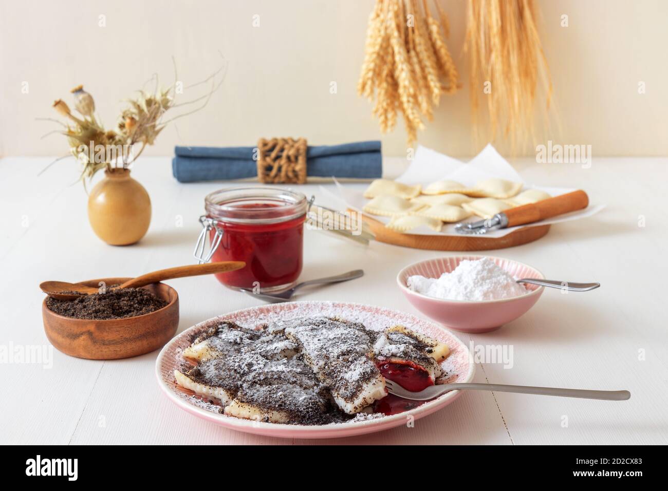 Pappstückchen gefüllt mit Pflaumenmarmelade, bestäubt mit Mohn und Puderzucker. Leckeres Dessert oder Hauptgericht mit Mohn. Weiße Holztisch Rückenplatte Stockfoto