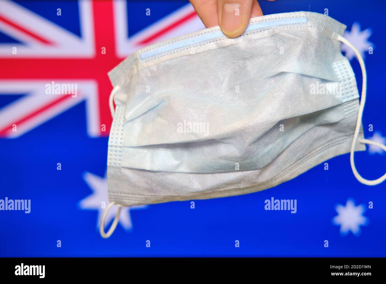 Eine Hand hält eine Maske vor dem Hintergrund der Flagge Australiens. Bekämpfung des Coronavirus in einer australischen Stadt Stockfoto