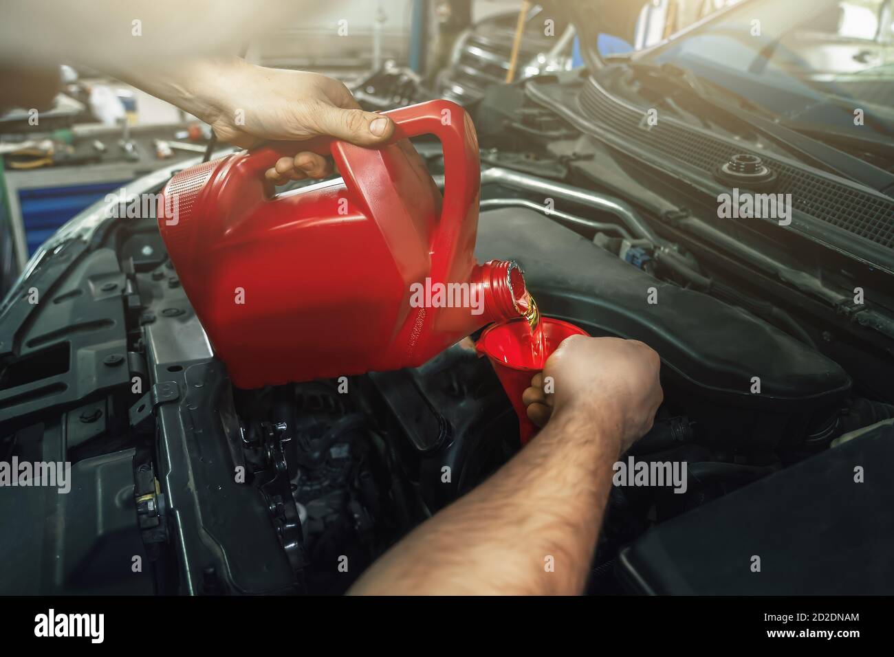Neues Motoröl aus dem Behälter in den Motortrichter bei der Fahrzeuginservicung aus nächster Nähe gießen. Stockfoto