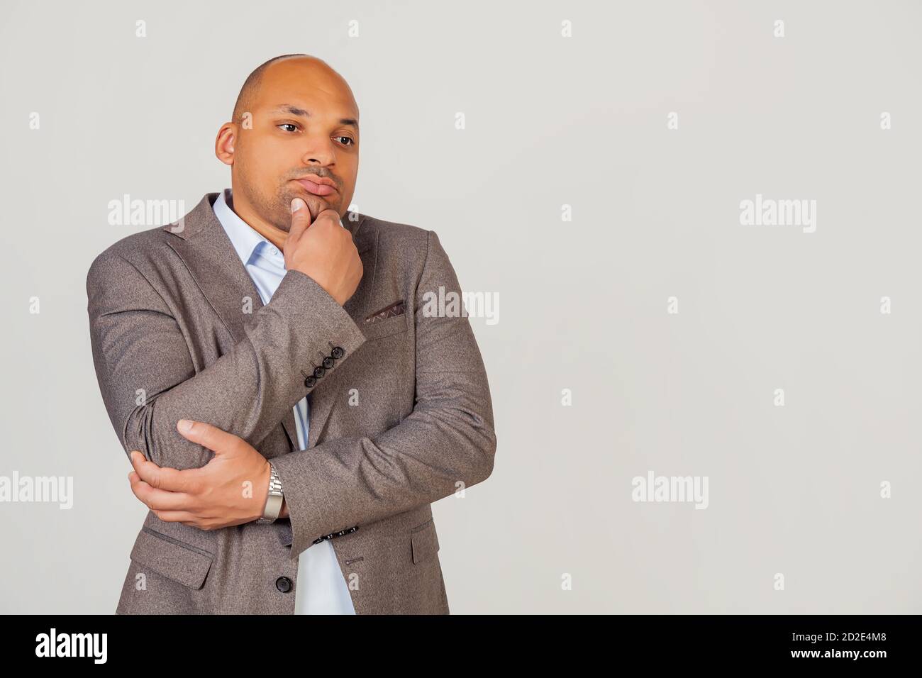 Hübscher junger afroamerikanischer Mann, Geschäftsmann in Jacke, der zur Seite schaut und denkt, das Kinn mit der Hand zu berühren, die zur Seite mit nachdenklichem Gesichtsausdruck schaut. Stockfoto