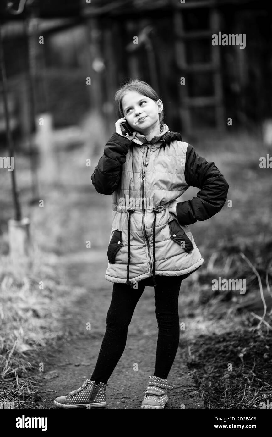 Kleine niedliche Mädchen im Gespräch auf Handy, im Freien im Dorf. Schwarzweiß-Fotografie. Stockfoto