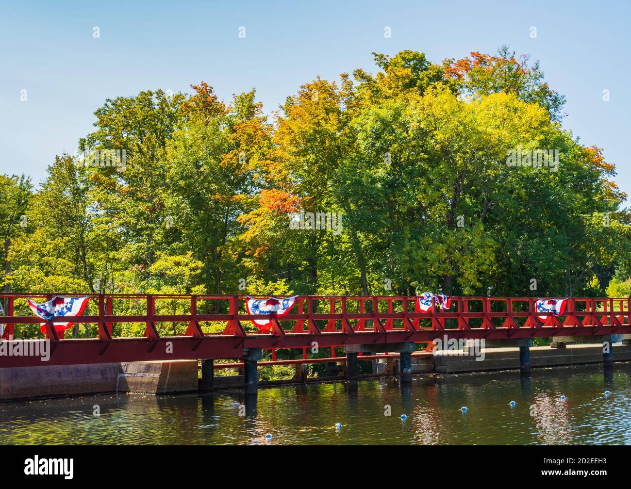 Fußgängerbrücke über einen Damm auf einem Teich mit patriotischen roten, weißen und blauen Fahnen weht in den Wind Stockfoto