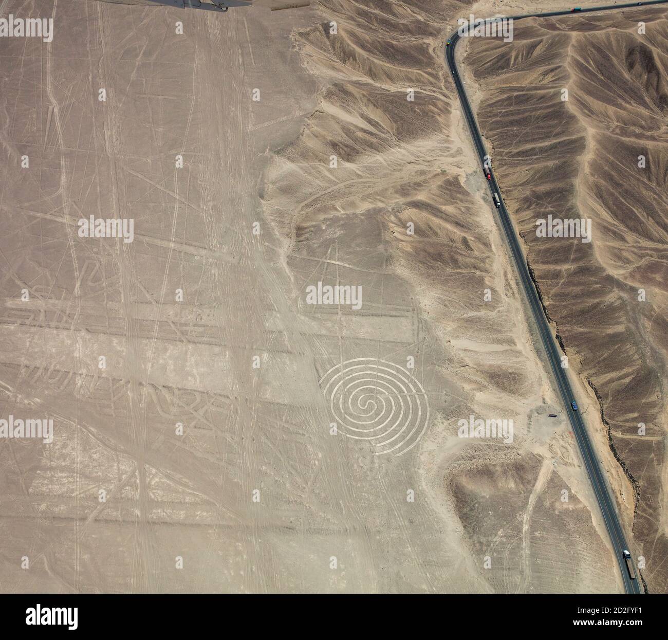 Lastwagen und Autos auf dem Pamamerican oder Inter-American Highway erweitern diese Luftaufnahme des Spiral-Geoglyps in den Nazca Lines, Peru. Stockfoto