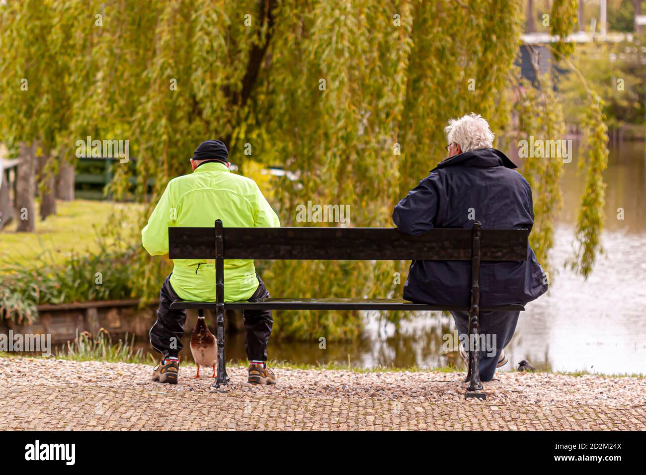 Ein junger Mann mit reflektierendem Outfit und Wintermütze und Ein älterer Mann mit grauen Haaren und Wintermantel sind Sitzen auf einer Holzbank am Avon Fluss in bat Stockfoto