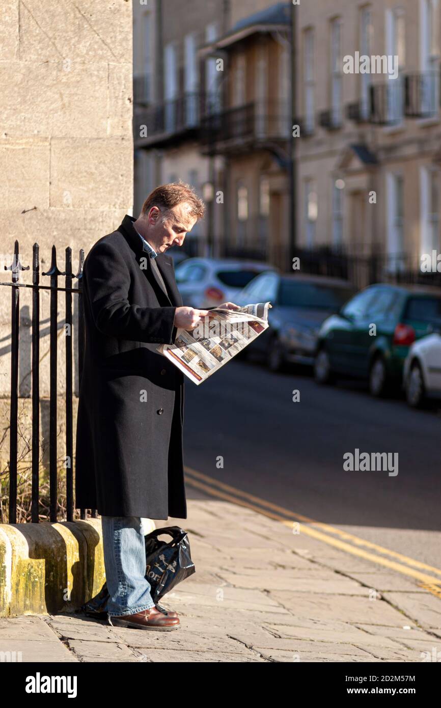 Bath, UK, 03/06/2010: Ein Kaukasier mittleren Alters, der einen langen Wintermantel trägt, steht morgens an einer Ecke und lehnt sich an Metallgeländer. Er ist c Stockfoto