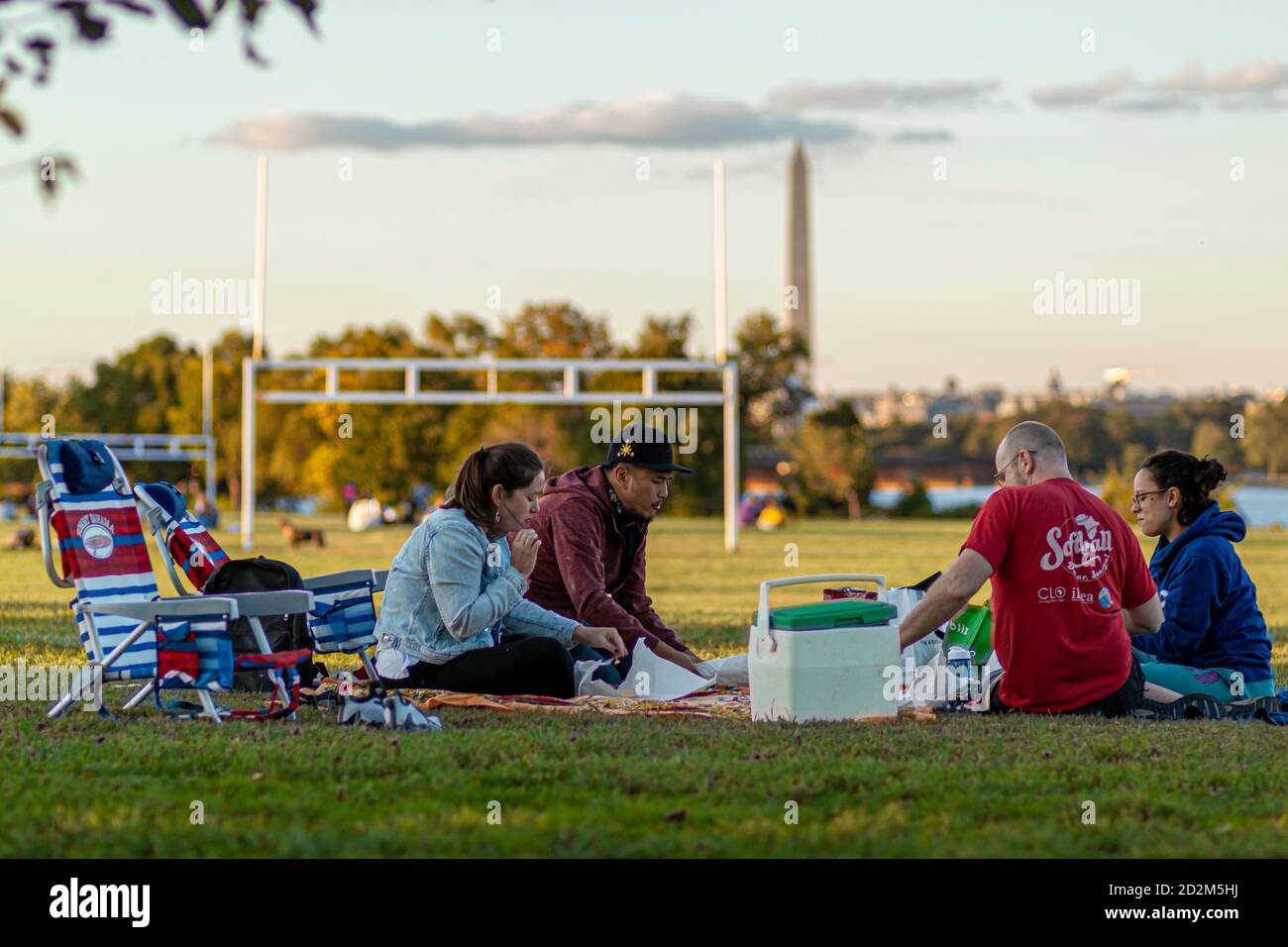 Arlington, VA, USA 10/02/2020: Eine multirassische Gruppe junger Menschen sitzen auf zusammenklappbaren Stühlen oder Laken auf dem Grasfeld des Gravelly Point Parks. Th Stockfoto