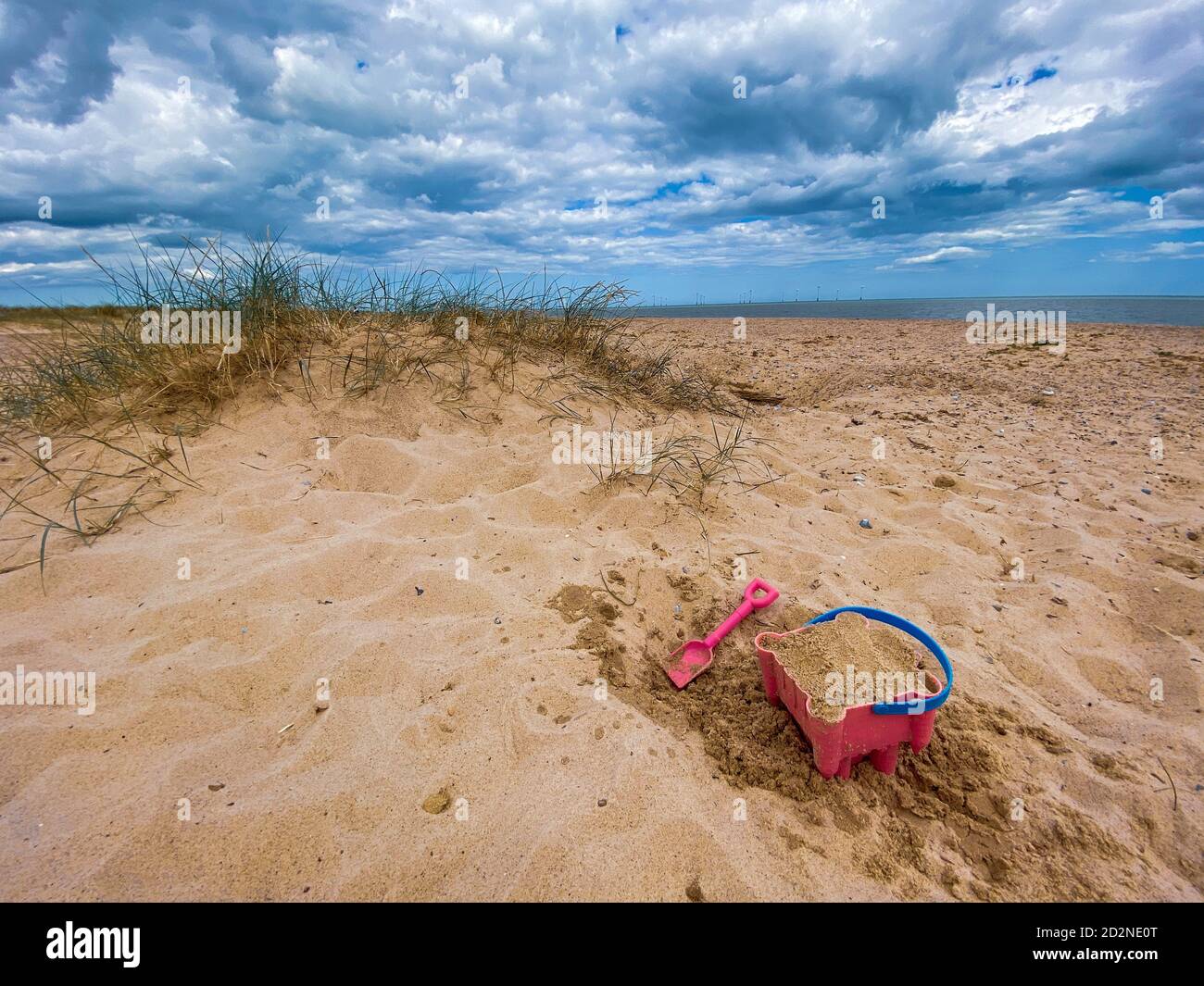 Pink Basket und Spaten auf Great Yarmouth Strand in einem kalten Sommertag, traditionelle englische Küste, Himmel mit Wolken keine Menschen, große Strecke des Sandes, Großbritannien sein Stockfoto